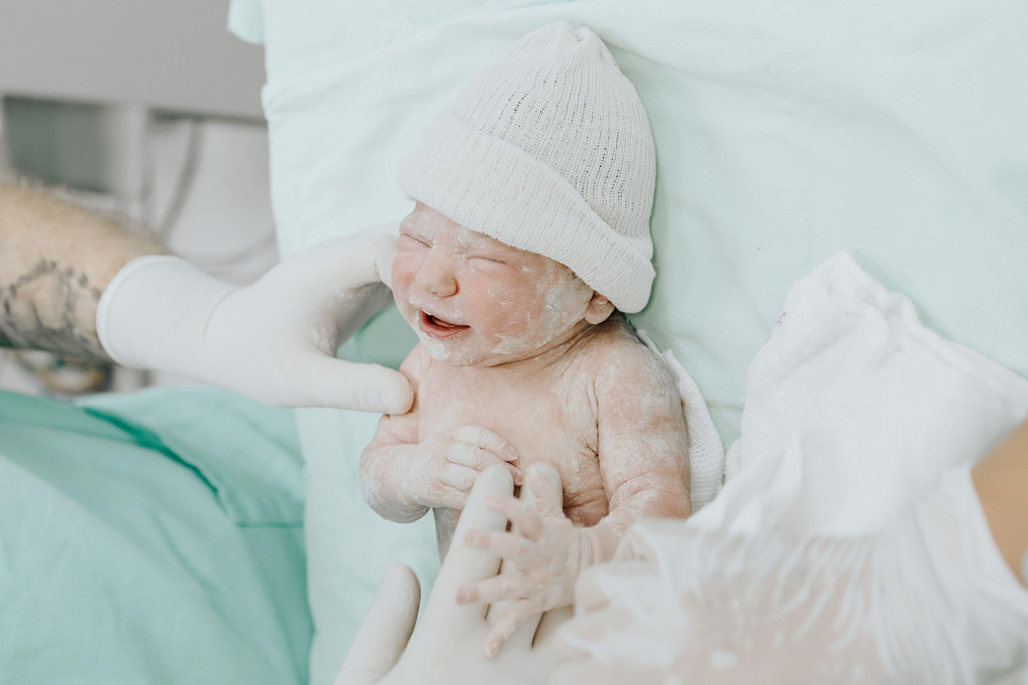 A newborn baby just delivered, attended by medical staff wearing gloves in a hospital setting.