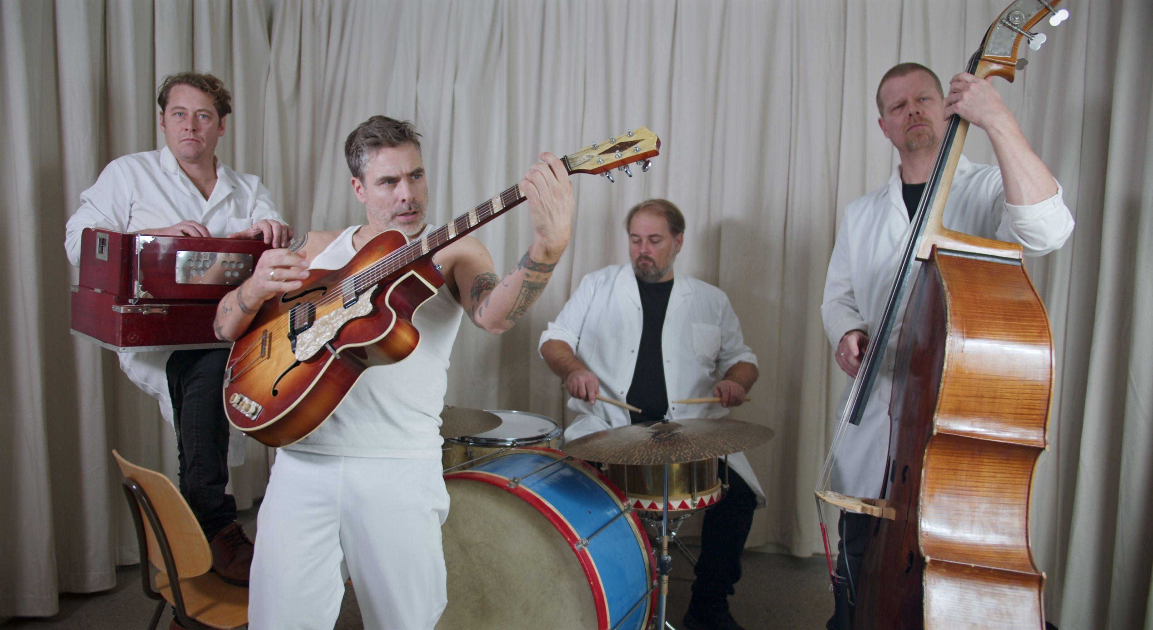 Group of musicians playing guitar, drums, and double bass indoors.