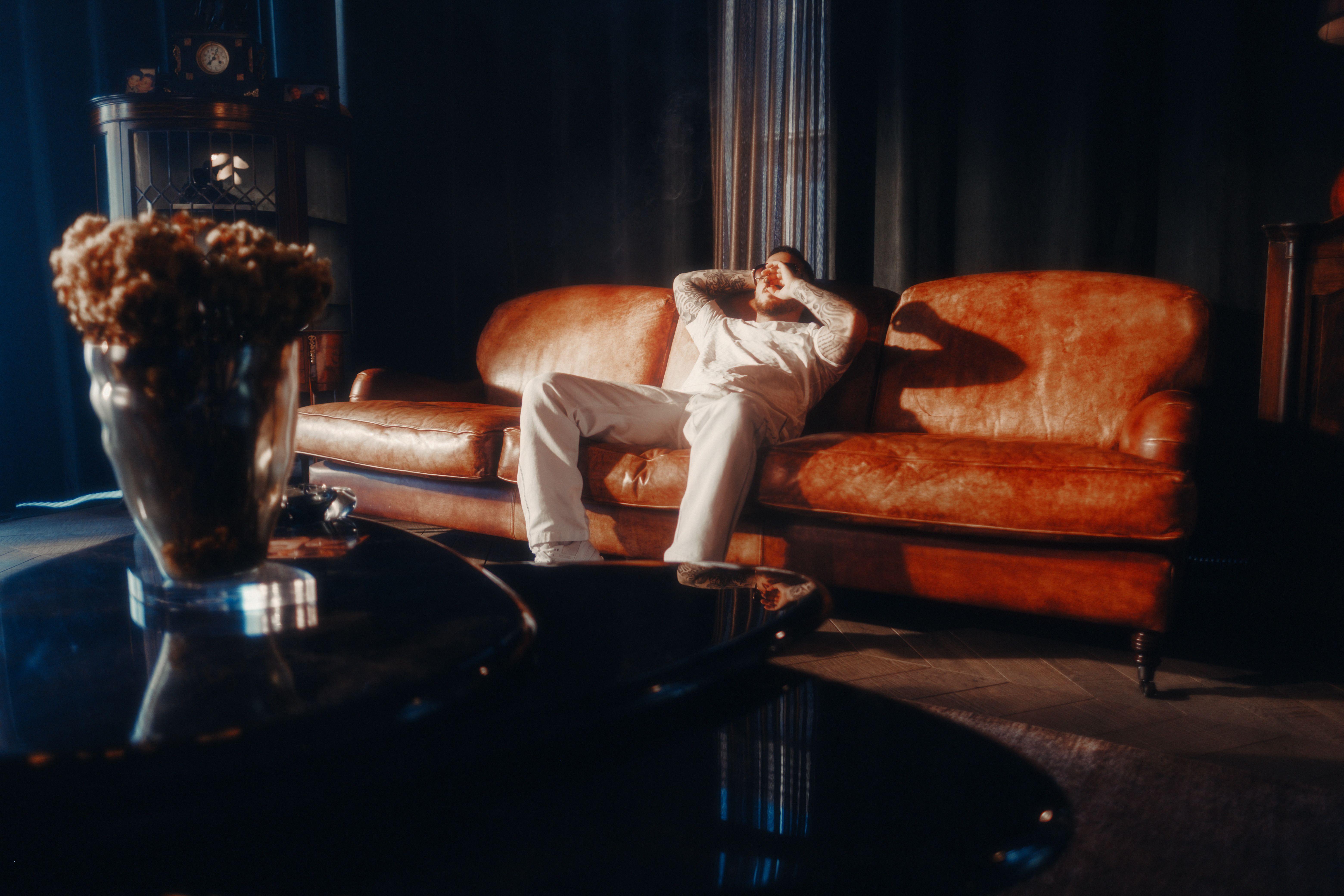 A man in a cozy living room relaxes on a vintage leather sofa, surrounded by warm ambient lighting.