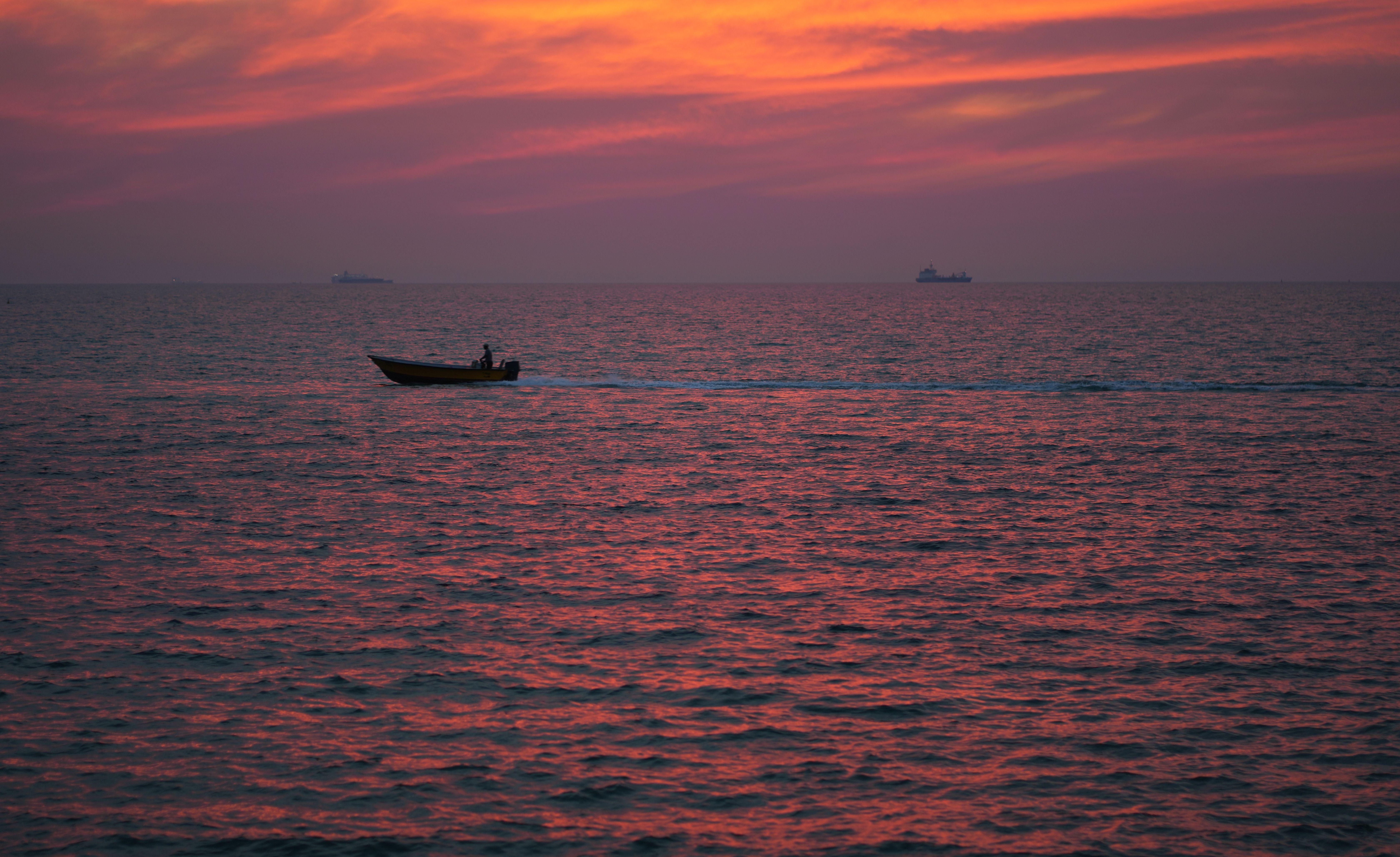 A lone boat navigates the vast ocean under a stunning red sunset sky.