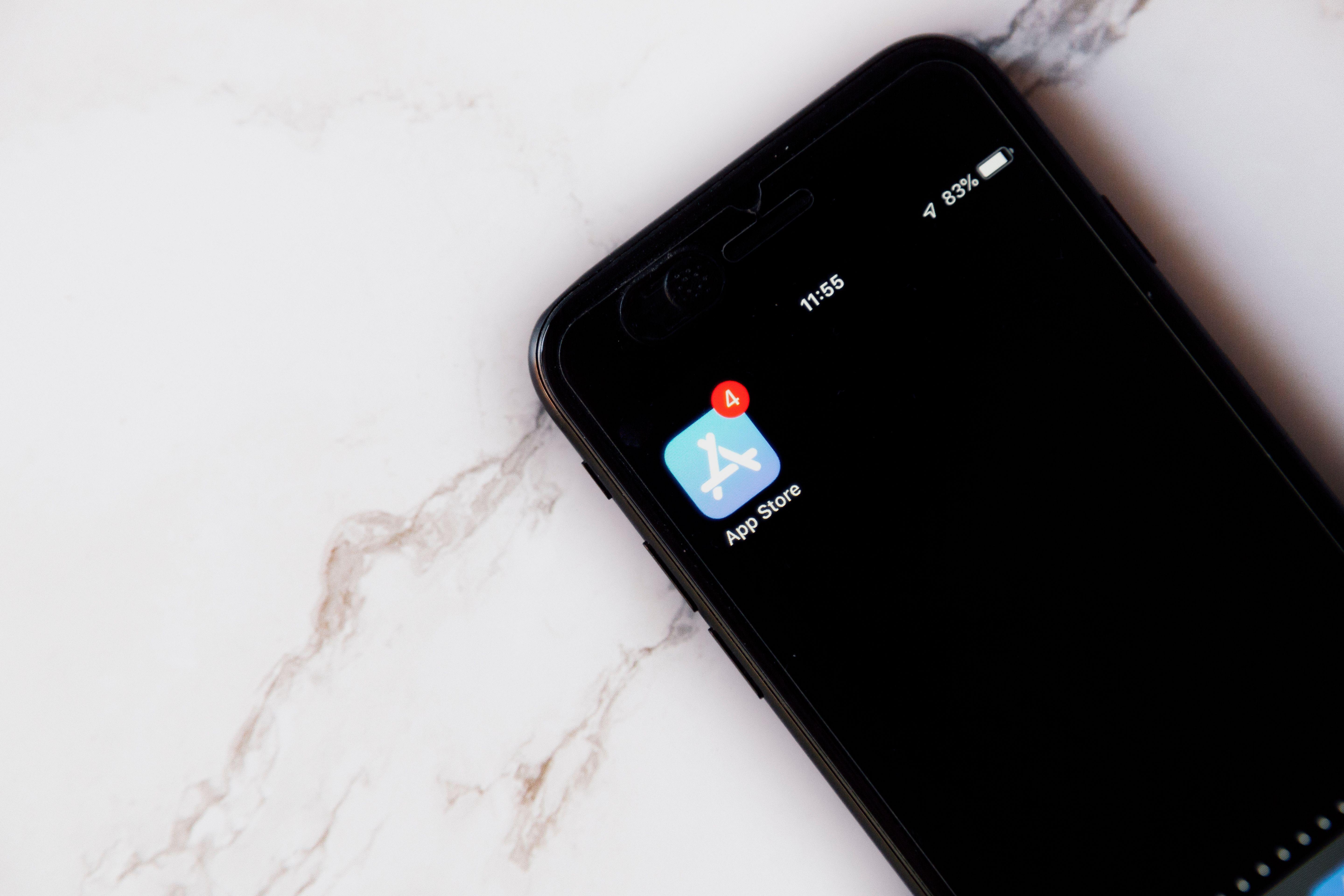 Close-up of an iPhone showing a notification on the App Store icon against a marble background.