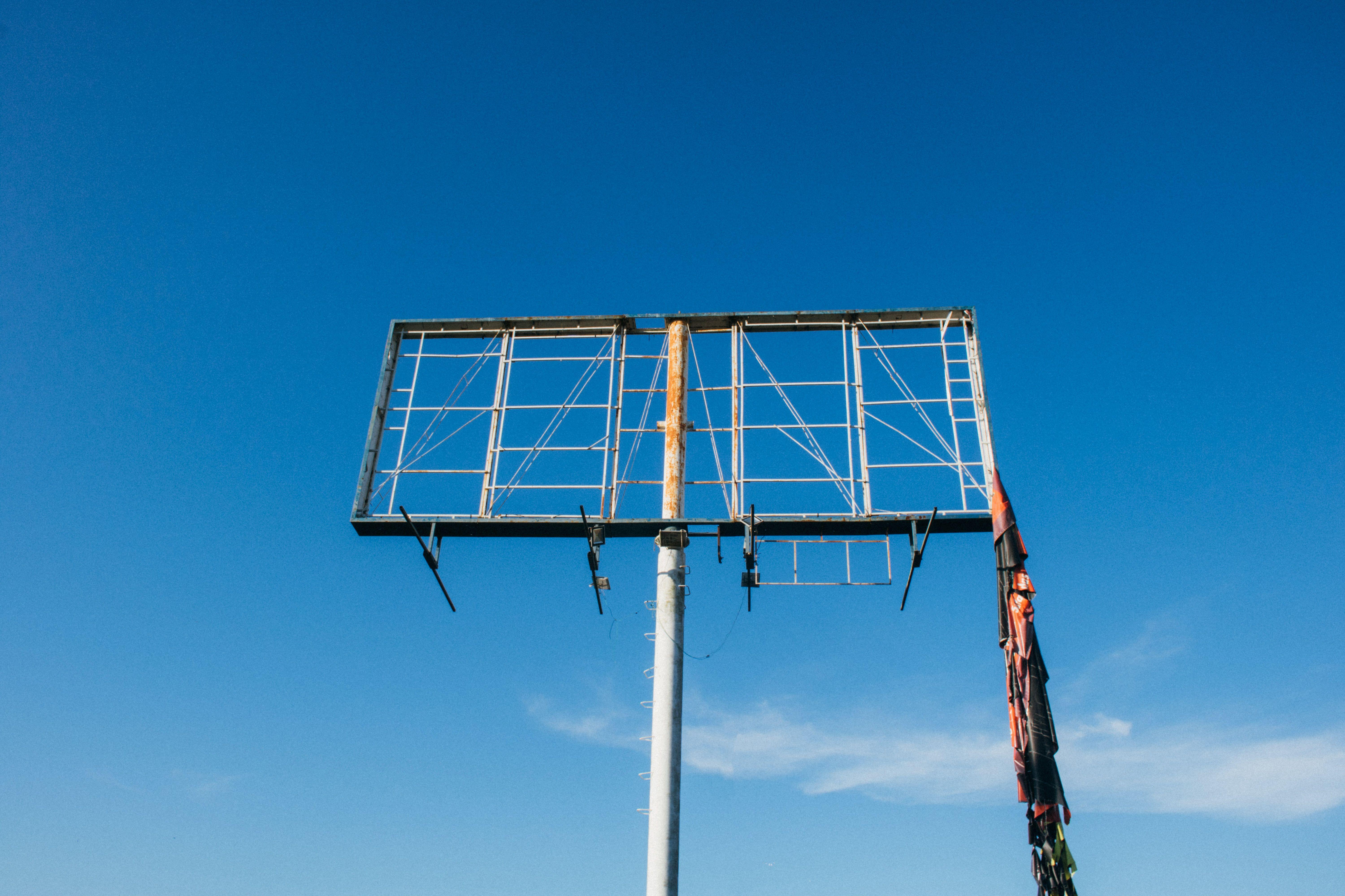 A rusty, empty billboard frame stands against a vast clear blue sky, symbolizing abandonment.