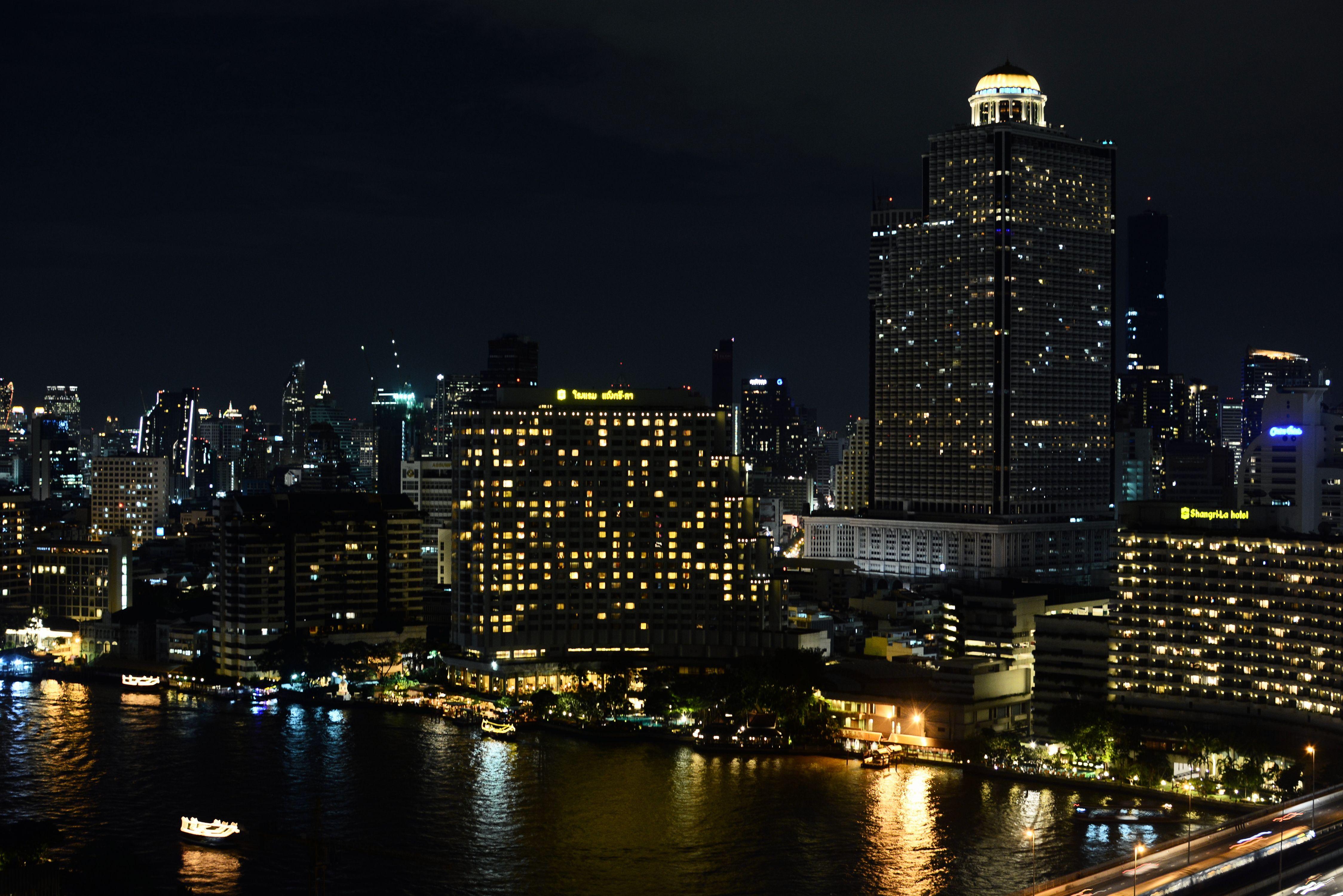 Explore the vibrant night skyline of Bangkok showcasing illuminated buildings along the riverfront, capturing the city's bustling spirit.