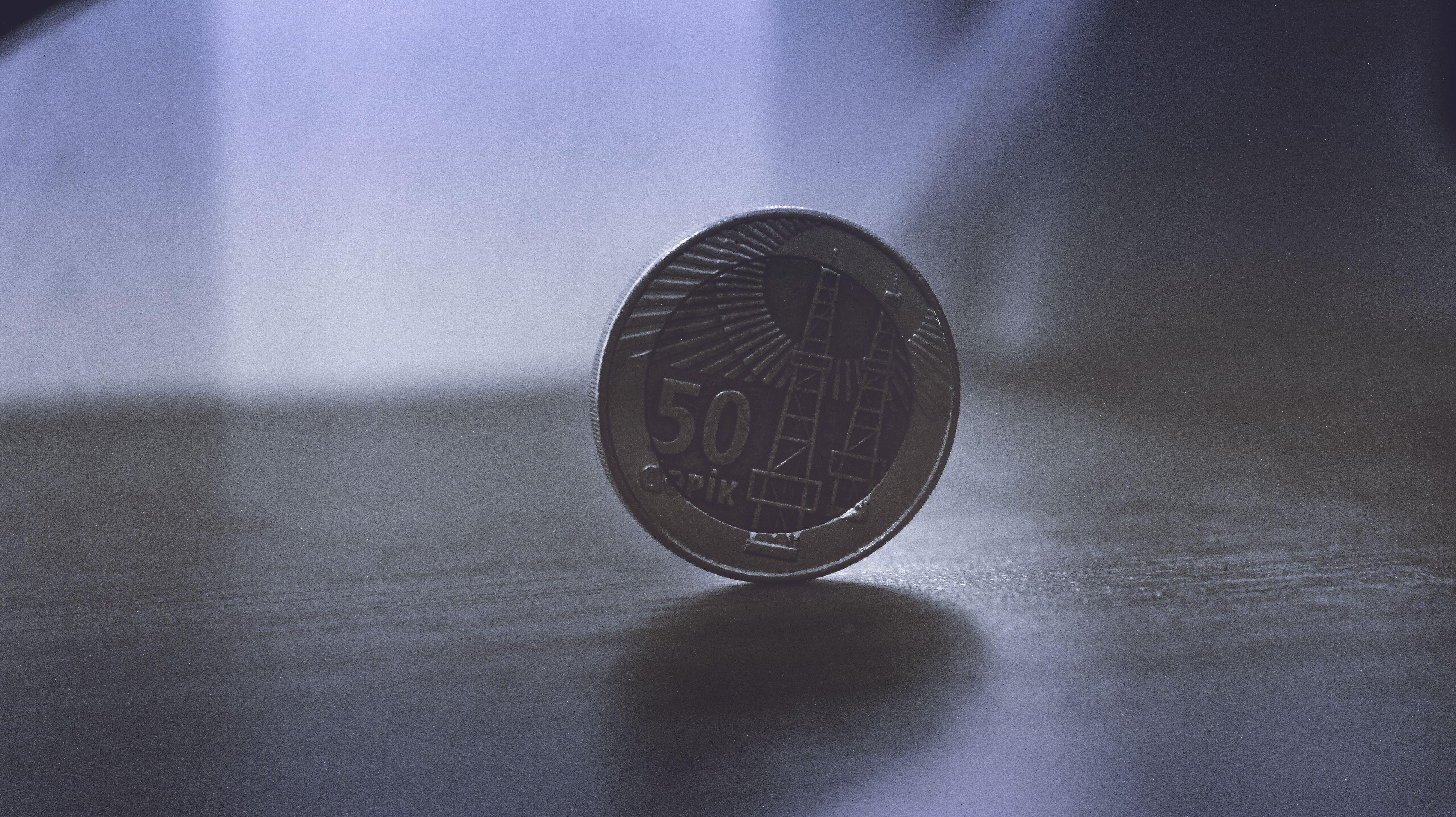 Close-up image of a 50 Qapik coin standing on a wooden surface, softly lit.