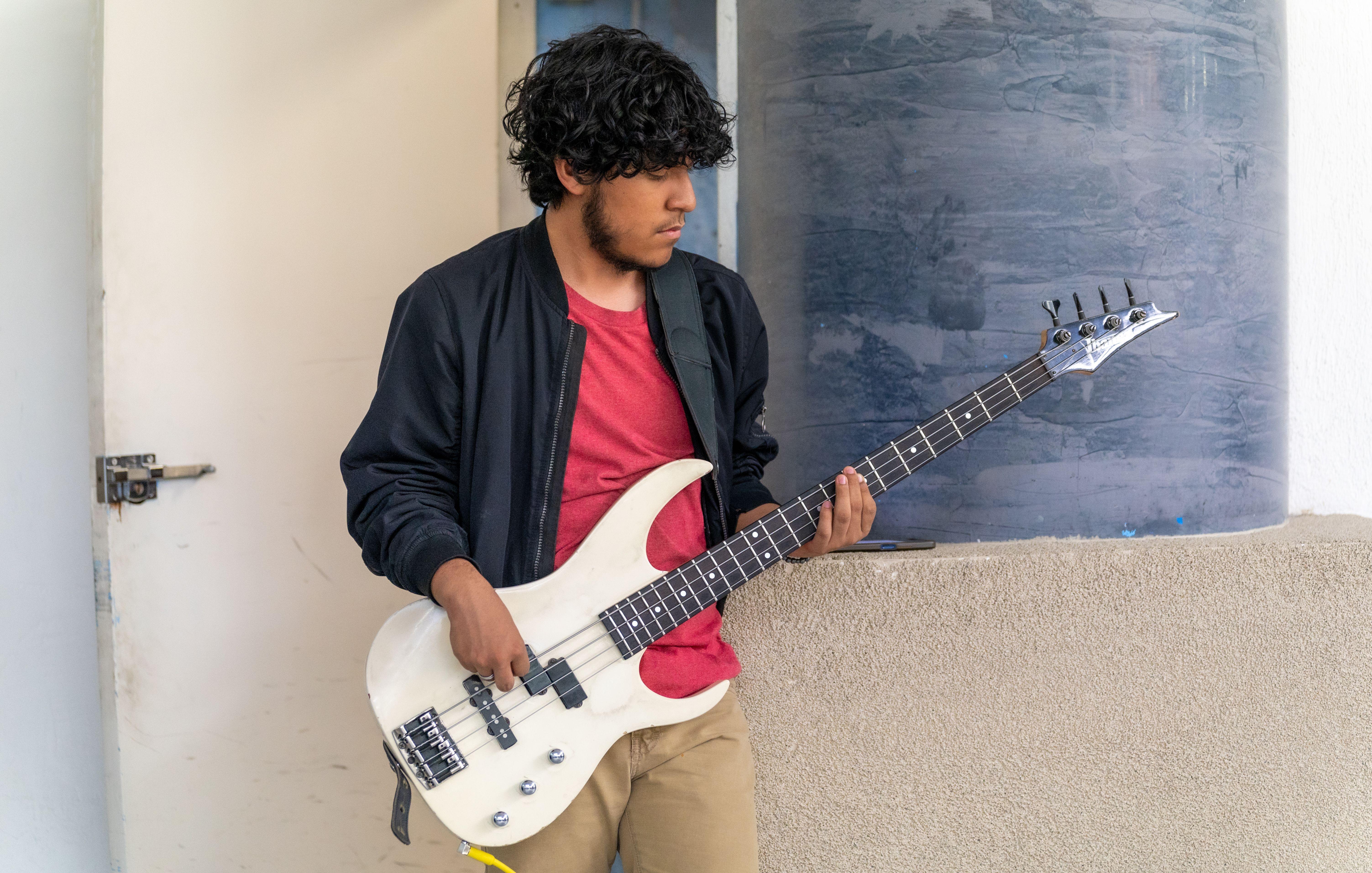 A young male musician playing an electric bass guitar outdoors in Ciudad de México.