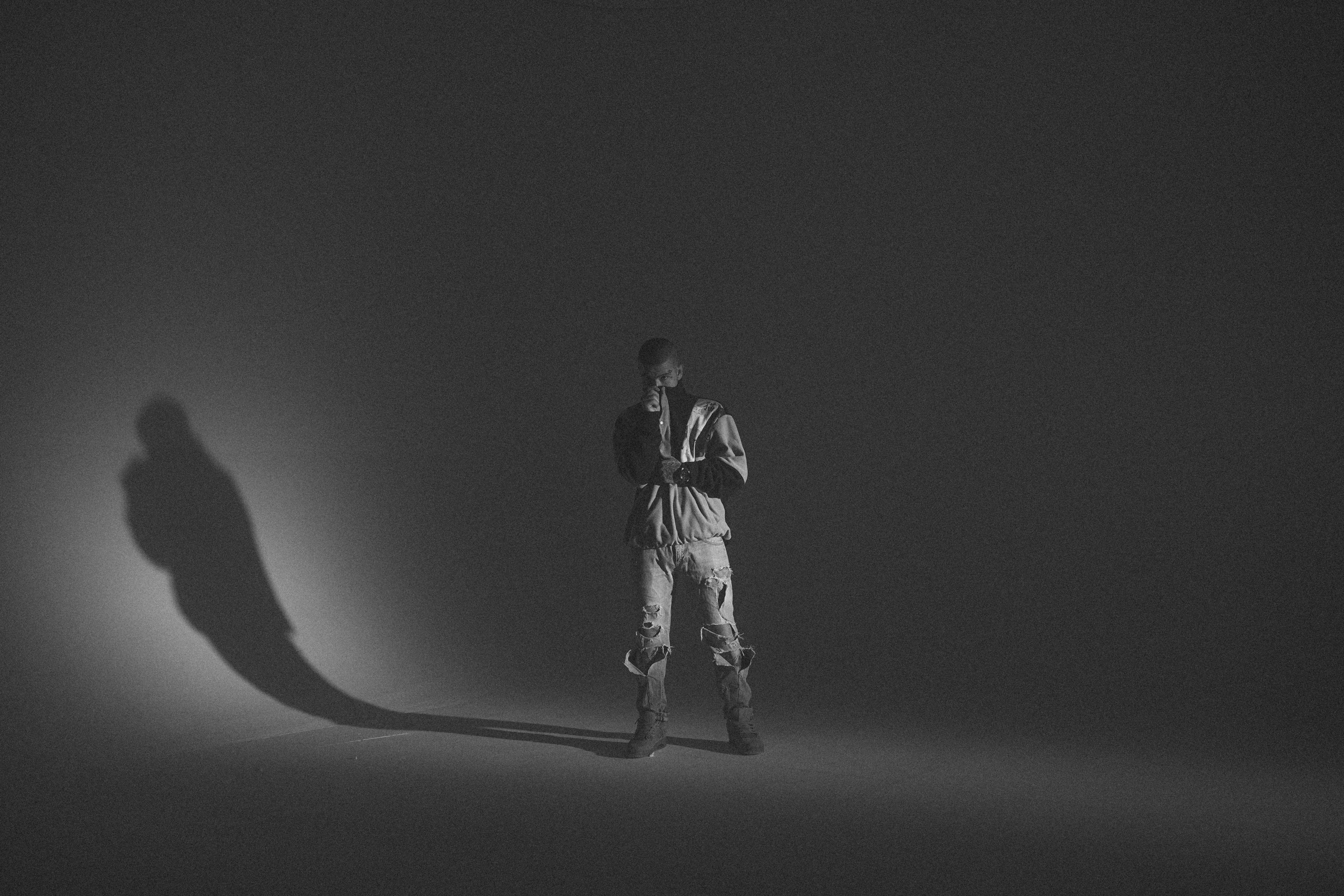 A monochrome portrait of a man in a studio setting, featuring bold shadows and casual fashion.