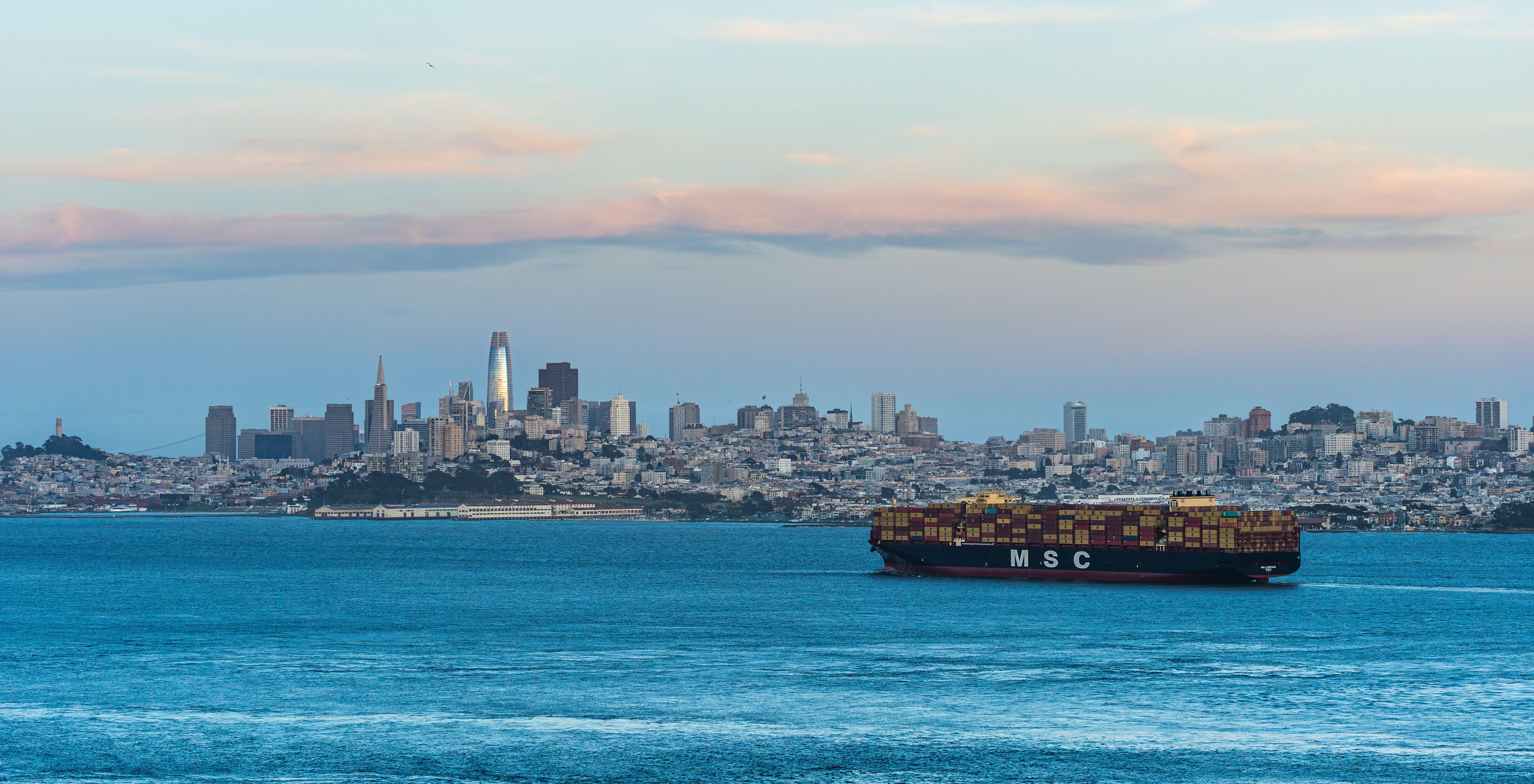A panoramic view of San Francisco's skyline with a cargo ship on the bay at dusk.