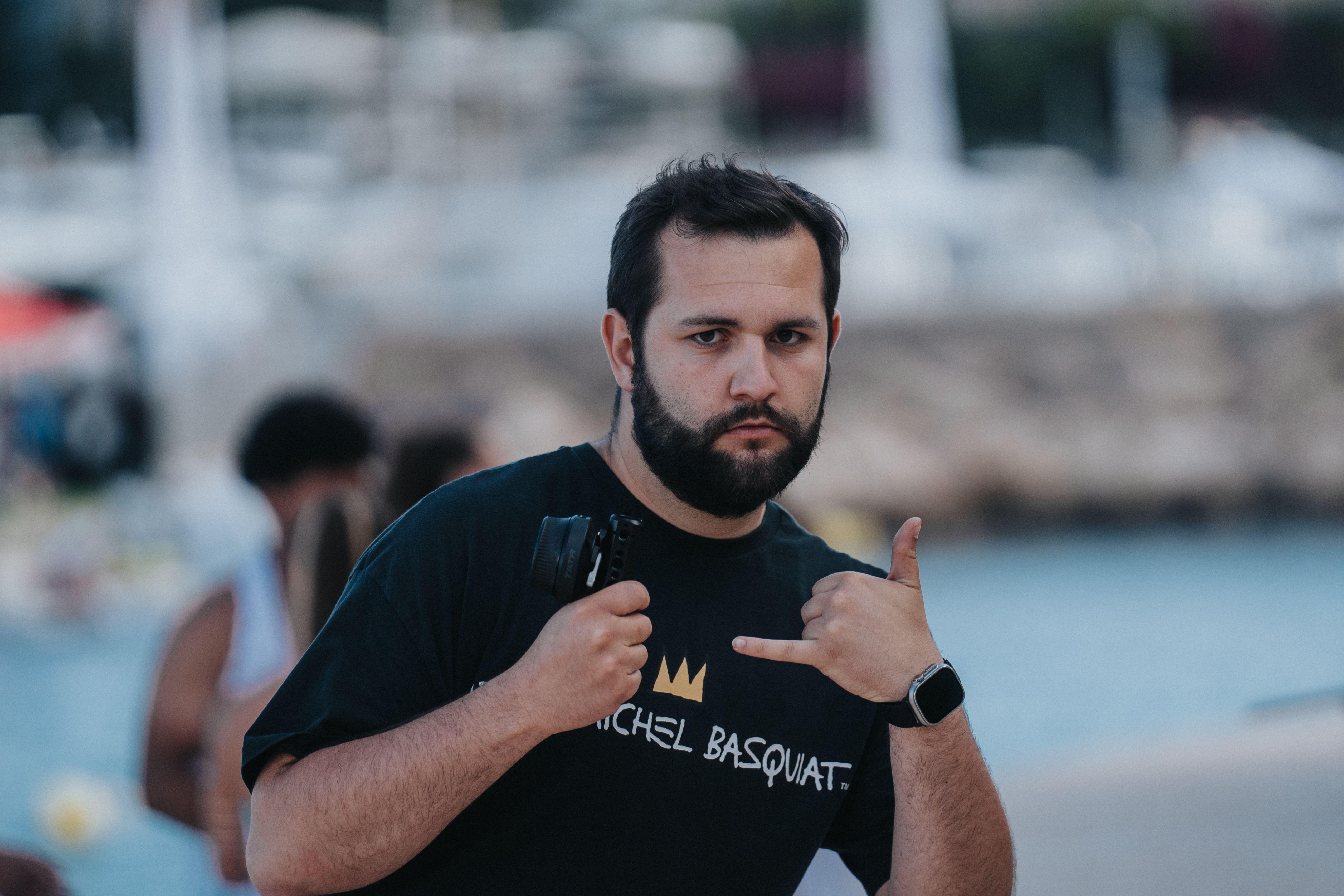 Man with a beard posing playfully with a camera at Palma harbor in summer.