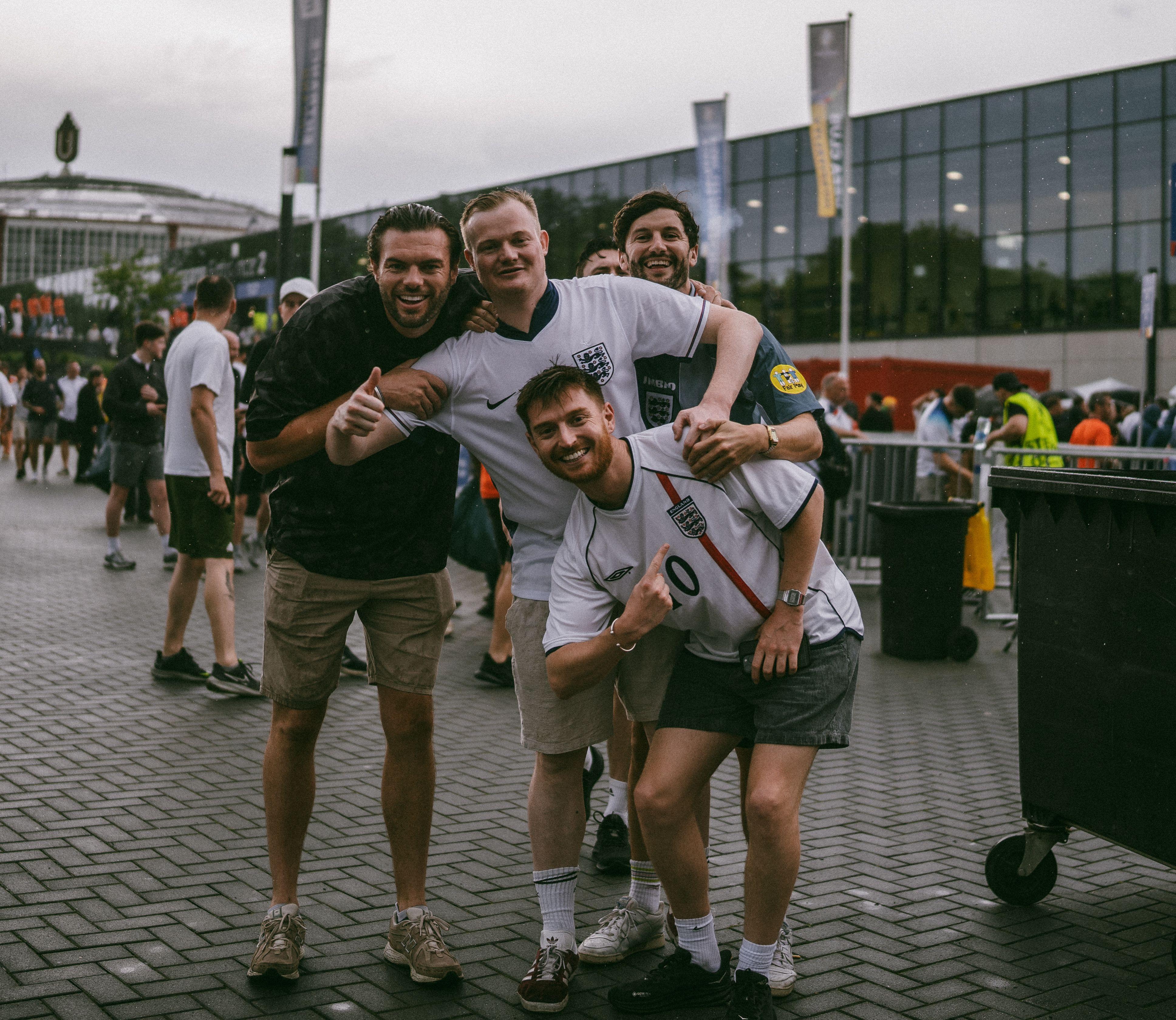 Group of enthusiastic football fans posing outside a stadium in England, showing camaraderie.
