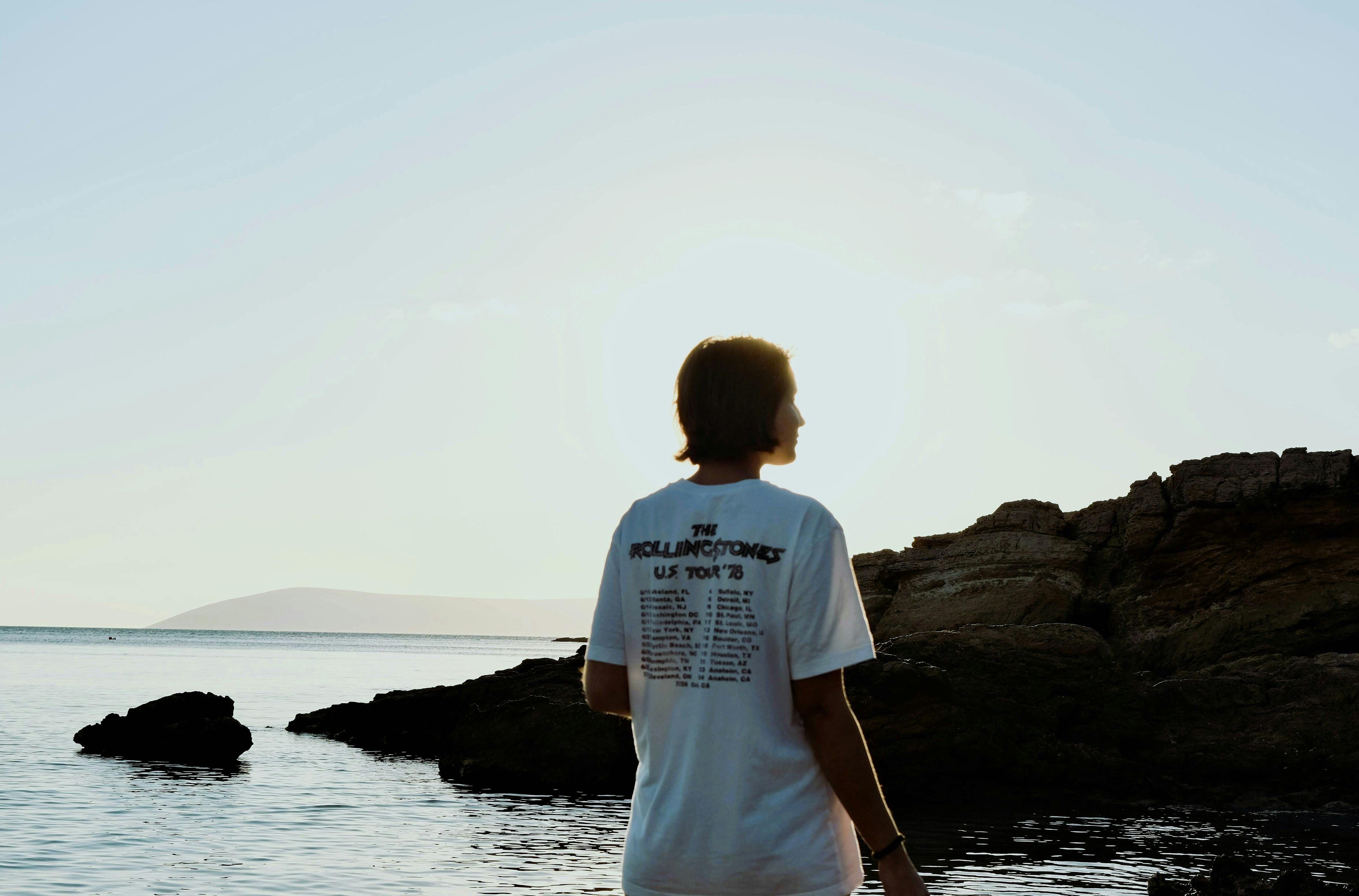 Silhouette of a person by the rocky seashore during sunset, serene ocean view.