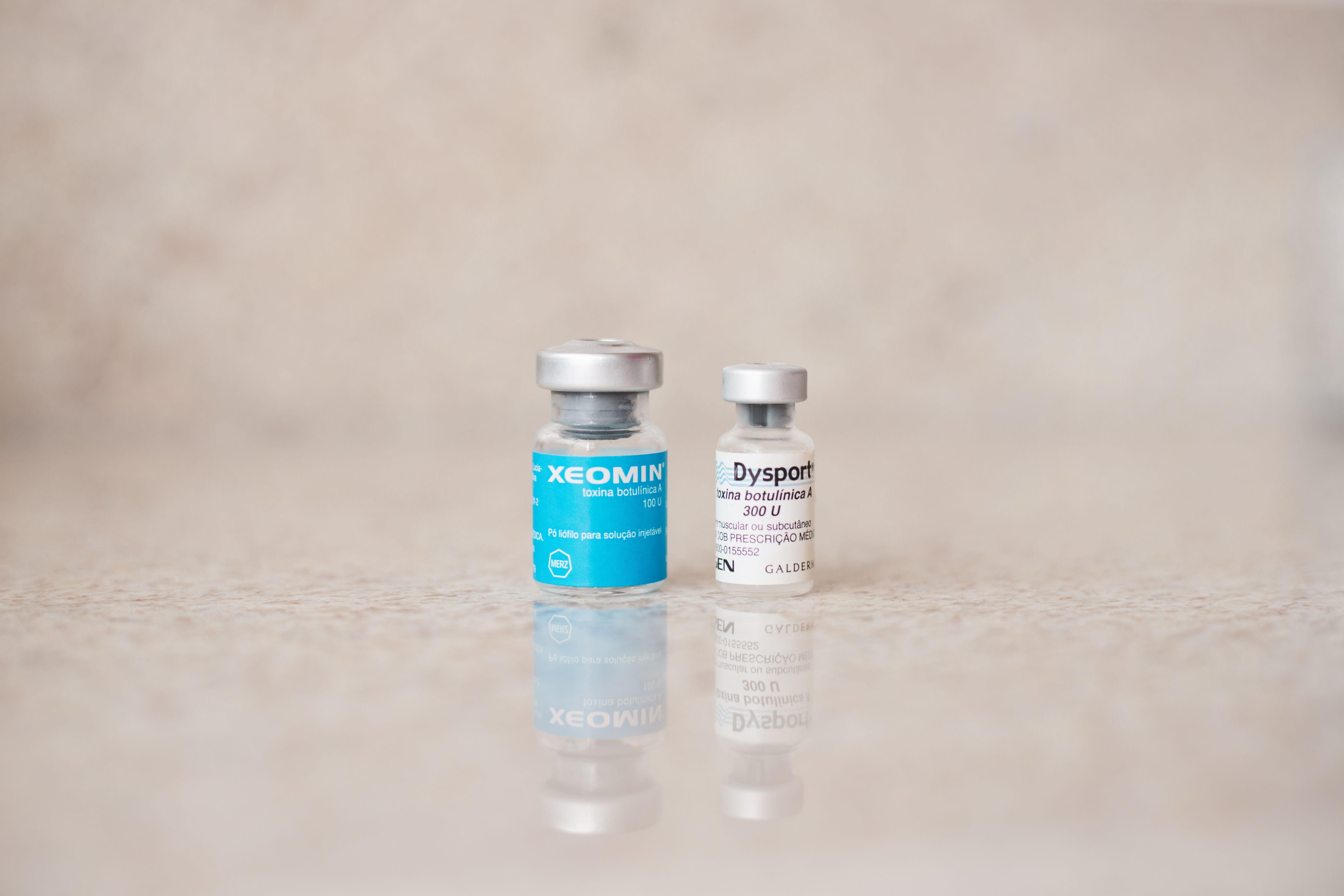 Close-up of Xeomin and Dysport bottles reflecting on a surface, shot indoors.