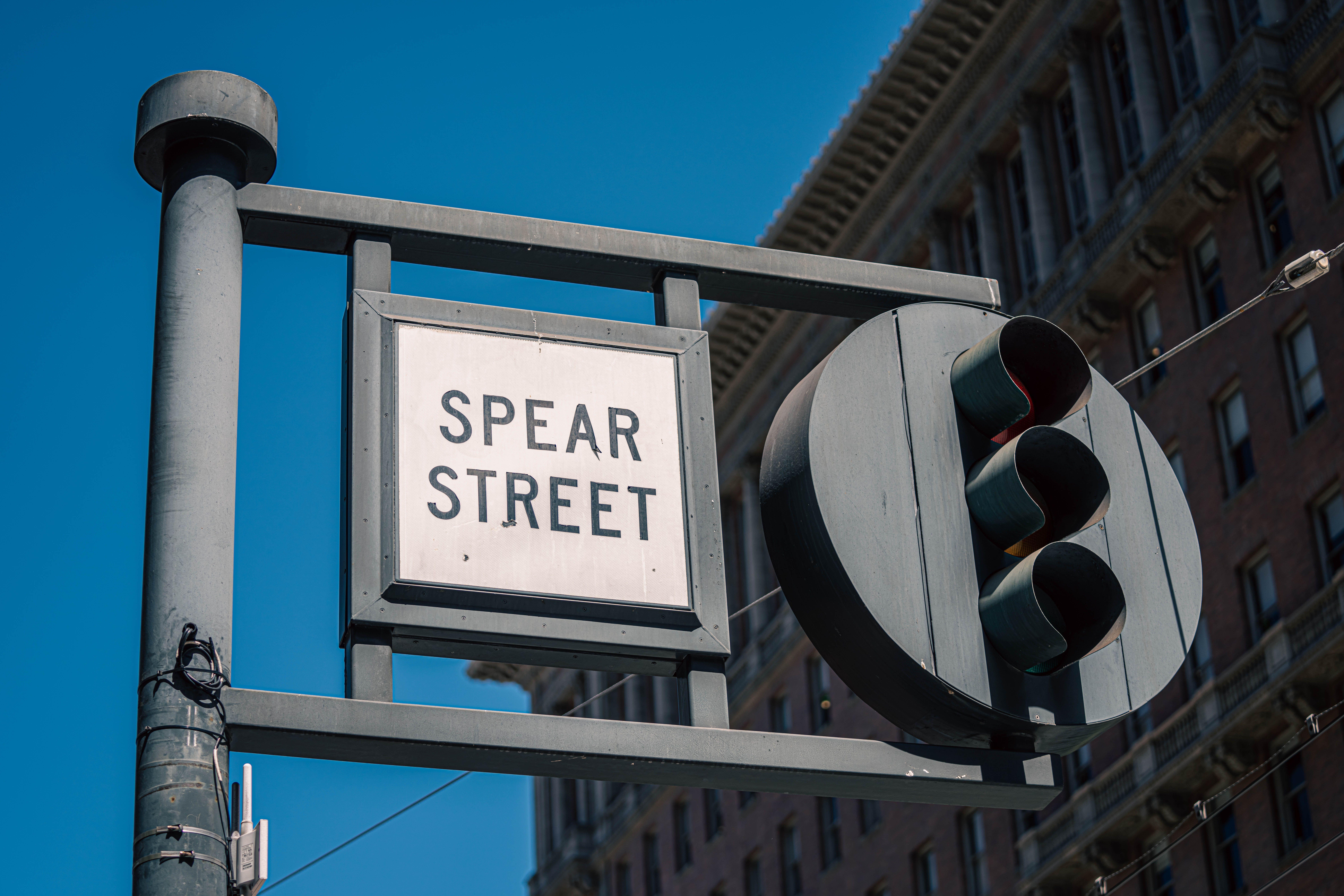 Traffic light and Spear Street sign with urban building backdrop in daylight.