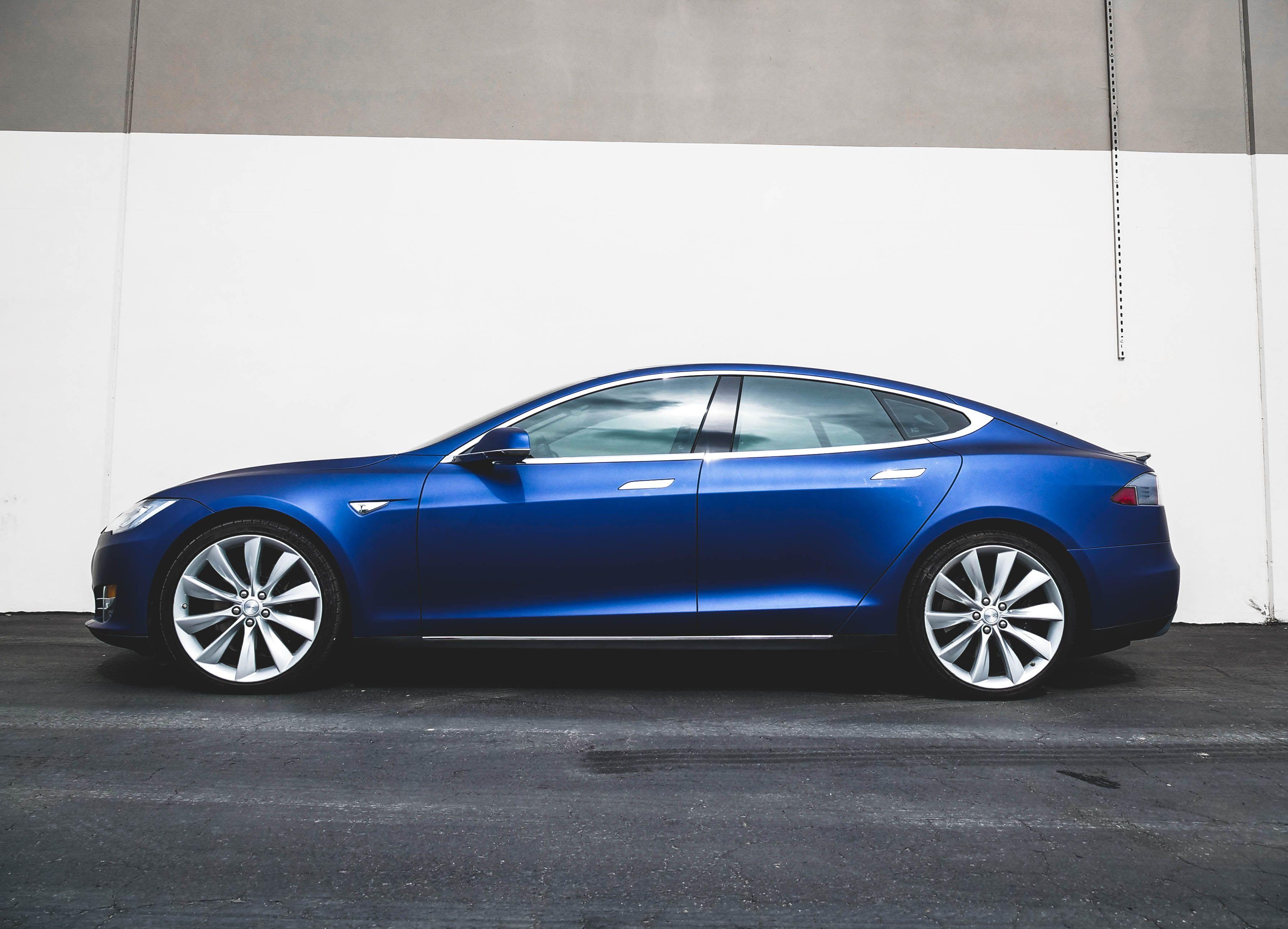 A modern blue electric car parked against a minimalist concrete wall, side view.