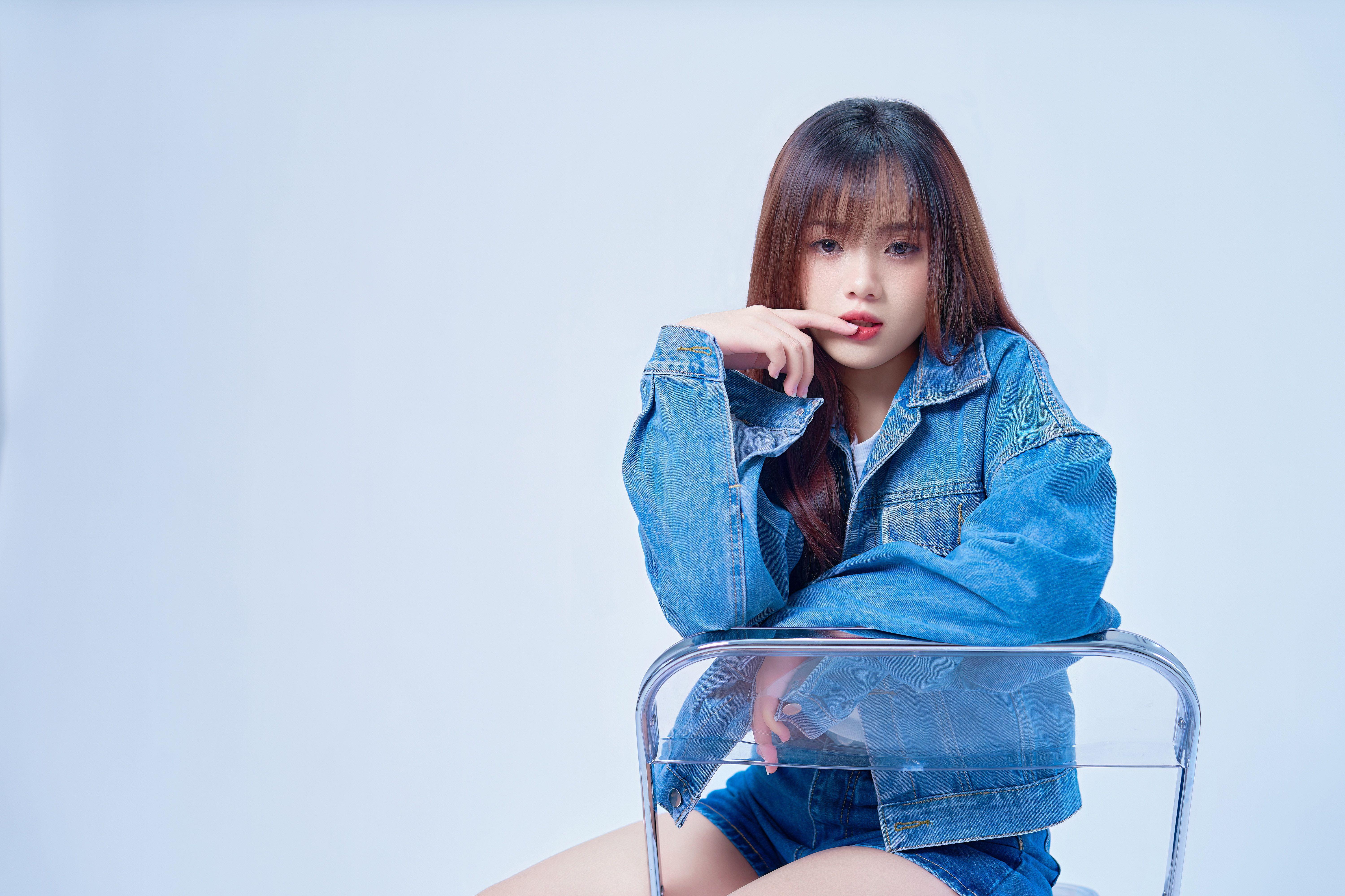 Studio portrait of a young woman in a denim jacket posing stylishly.