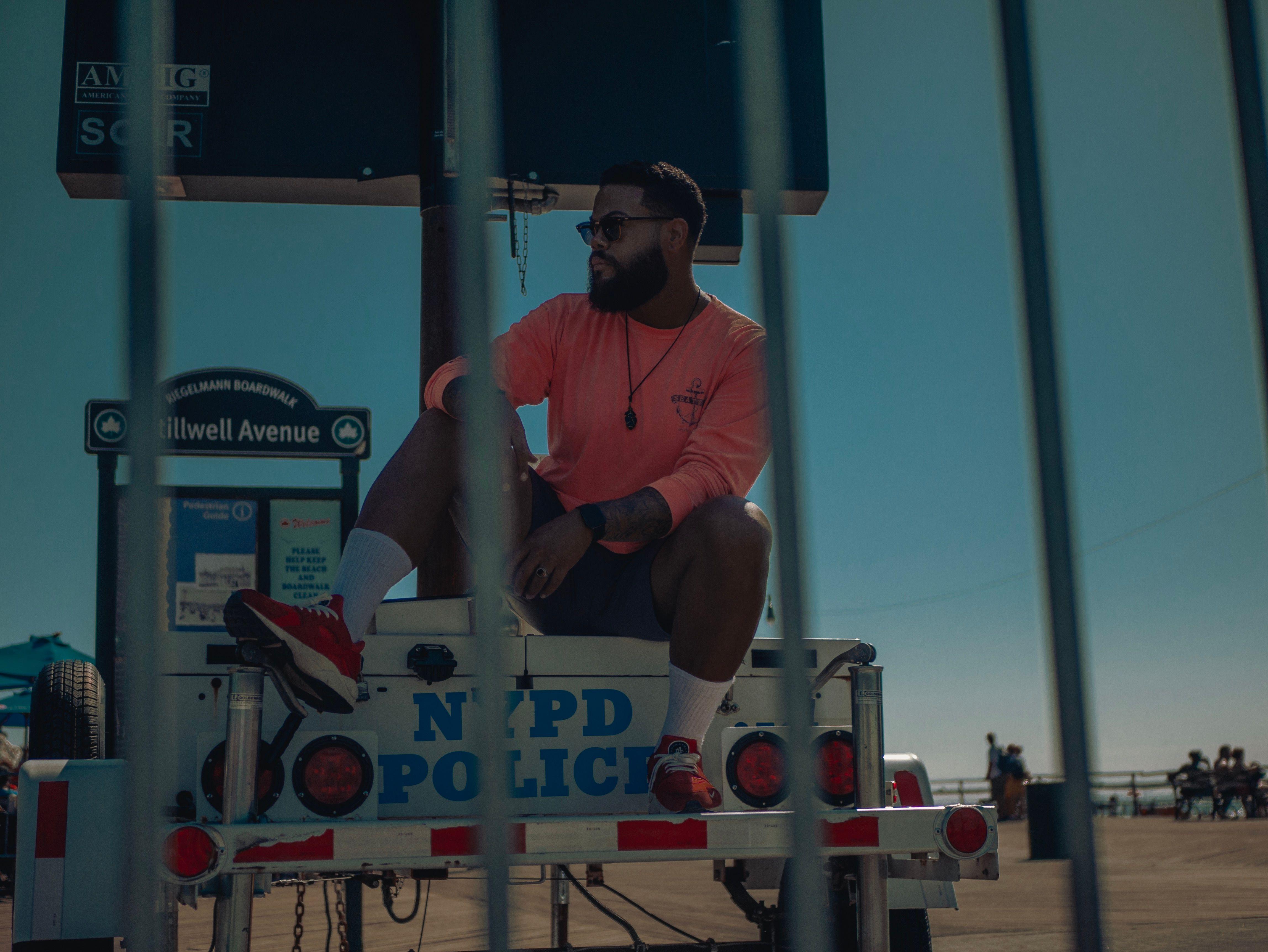 Stylish man in sunglasses poses on an NYPD vehicle at Coney Island boardwalk, NYC.