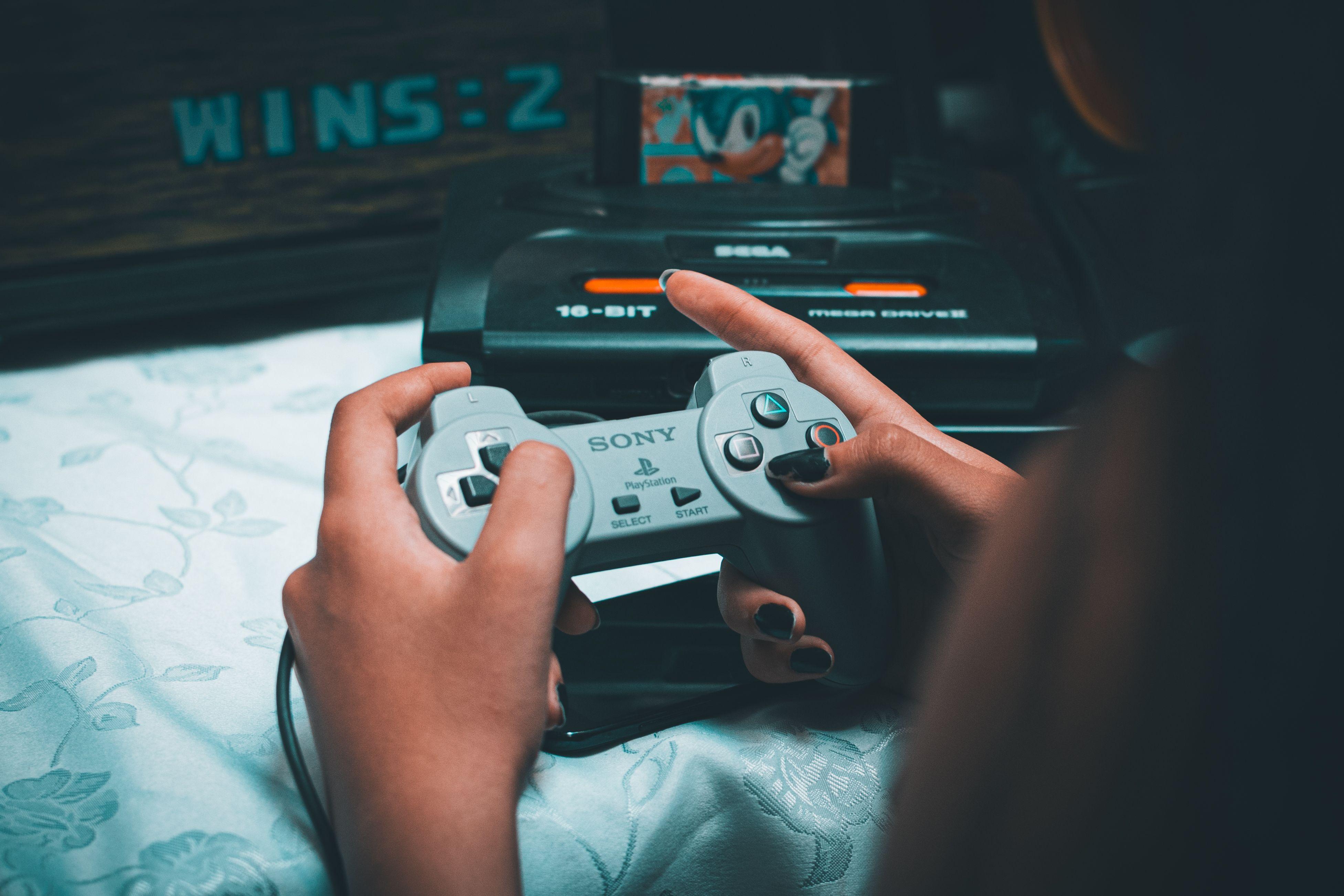 Close-up of hands holding vintage Sony controller with Sega Mega Drive in background.