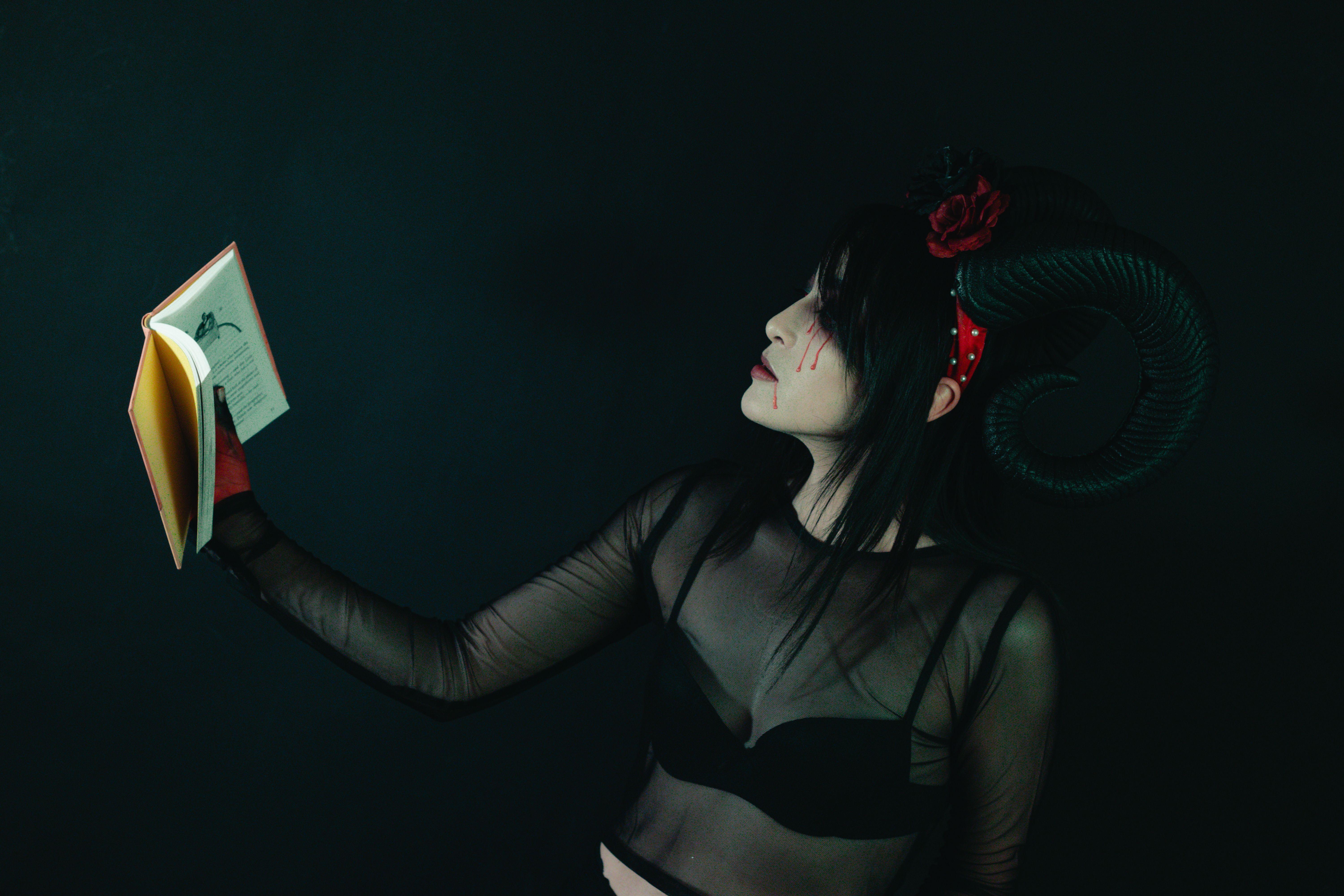 Artistic portrait of a woman in a horned costume holding a book, evoking a dark fantasy theme.