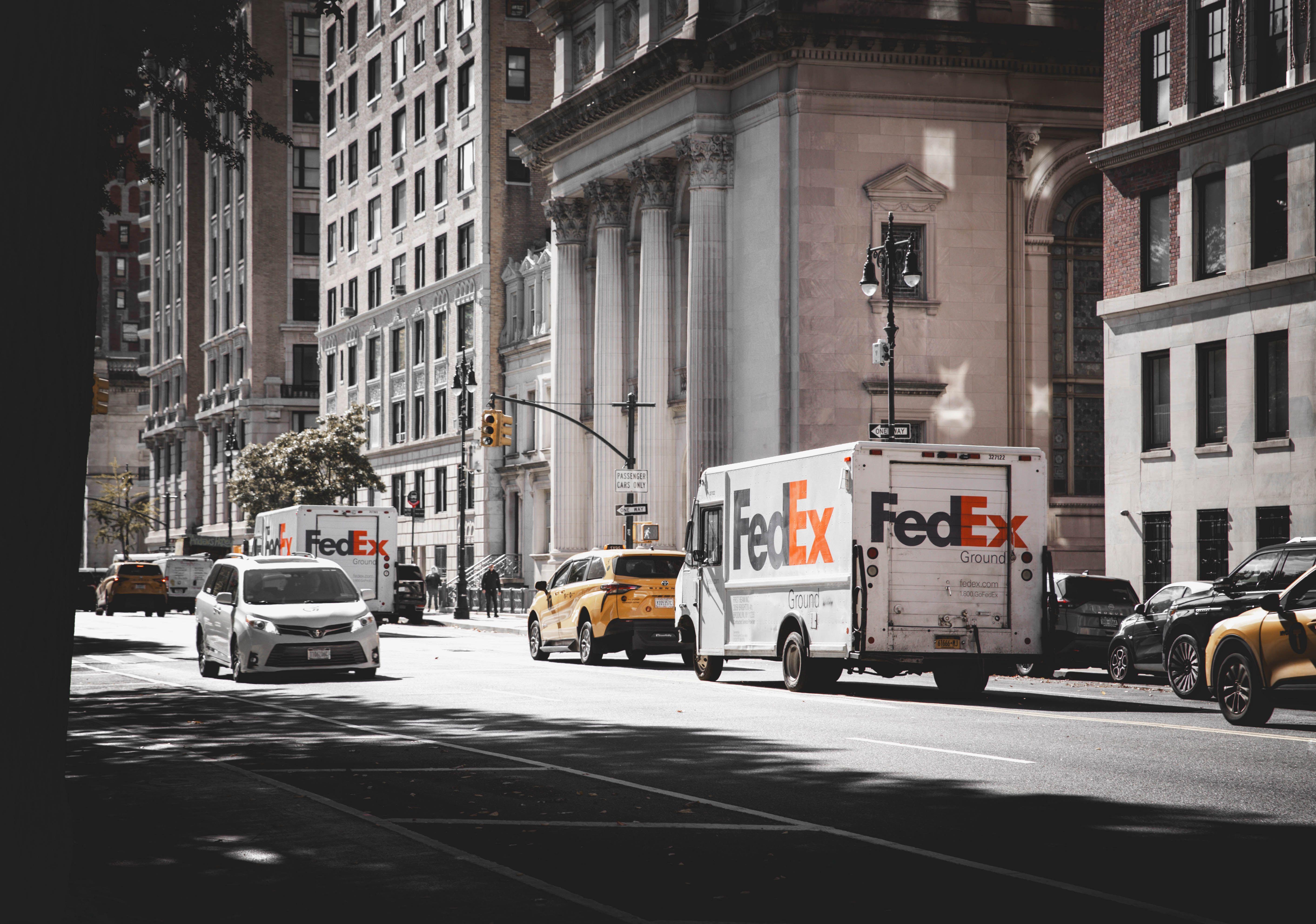 Busy street in New York City with delivery vans and cars in front of historic architecture.