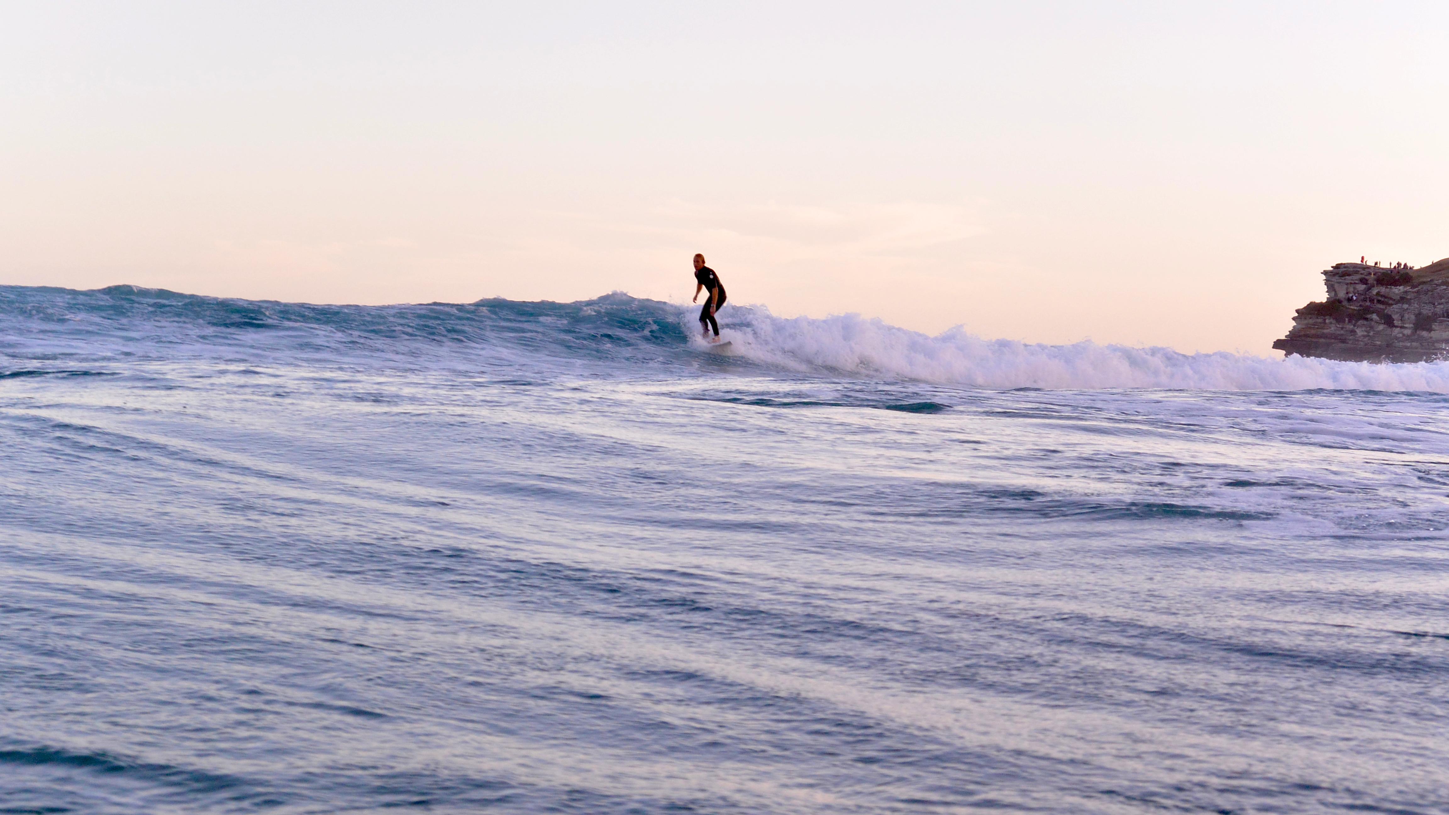 Capture the thrill of surfing with a lone surfer conquering waves at Bondi Beach during a stunning sunset.