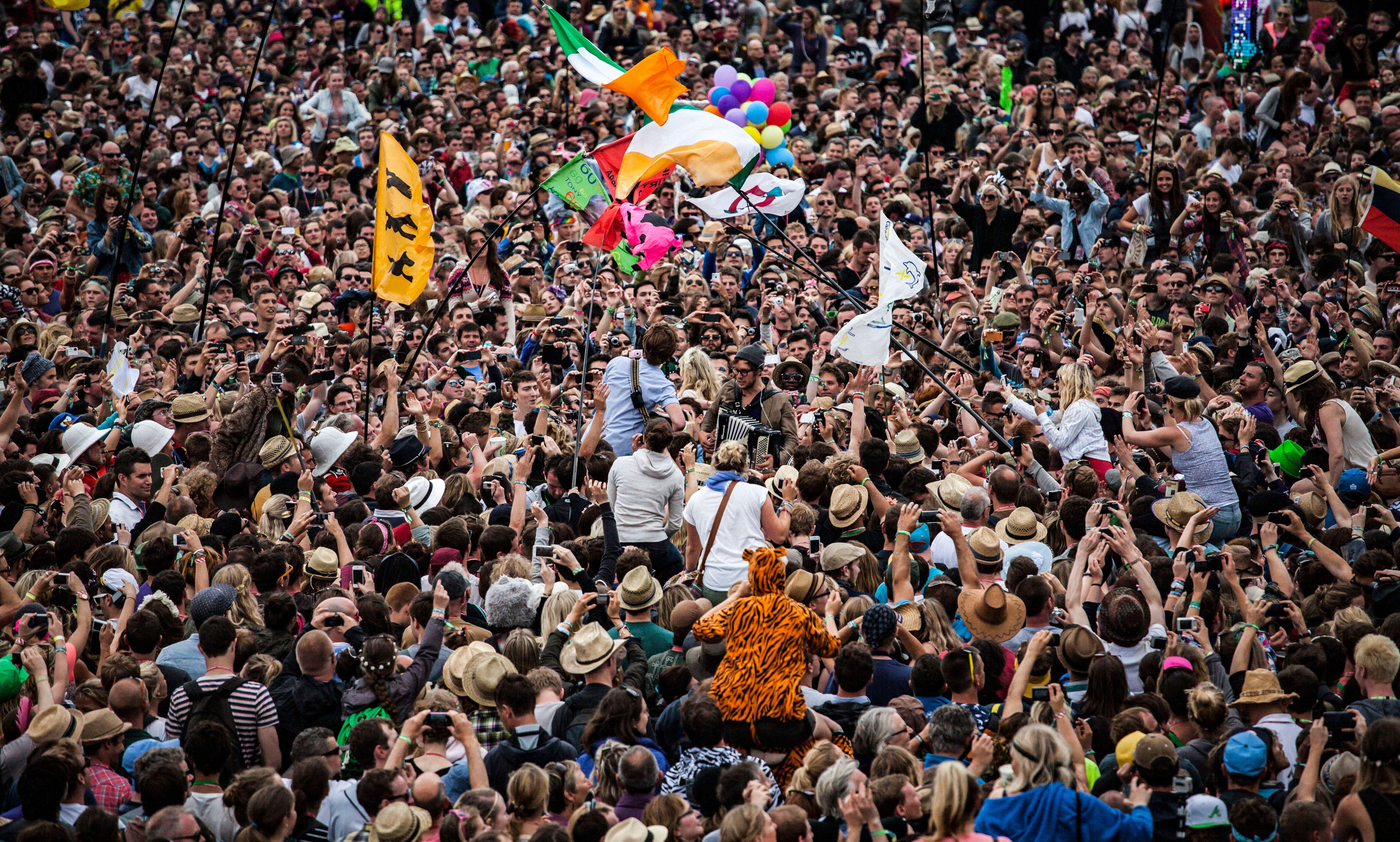 A lively festival scene with a large crowd, flags, and live music.