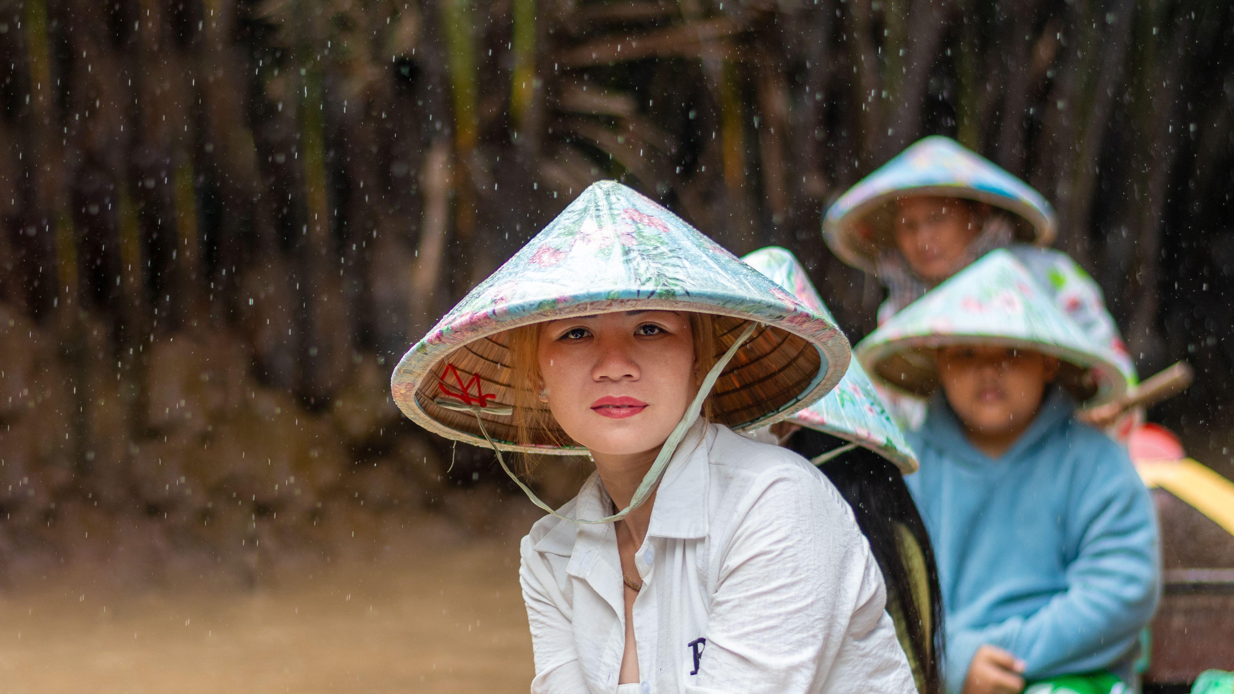 A scene of people wearing traditional hats during a rainy boat ride in Mỹ Tho, Vietnam.