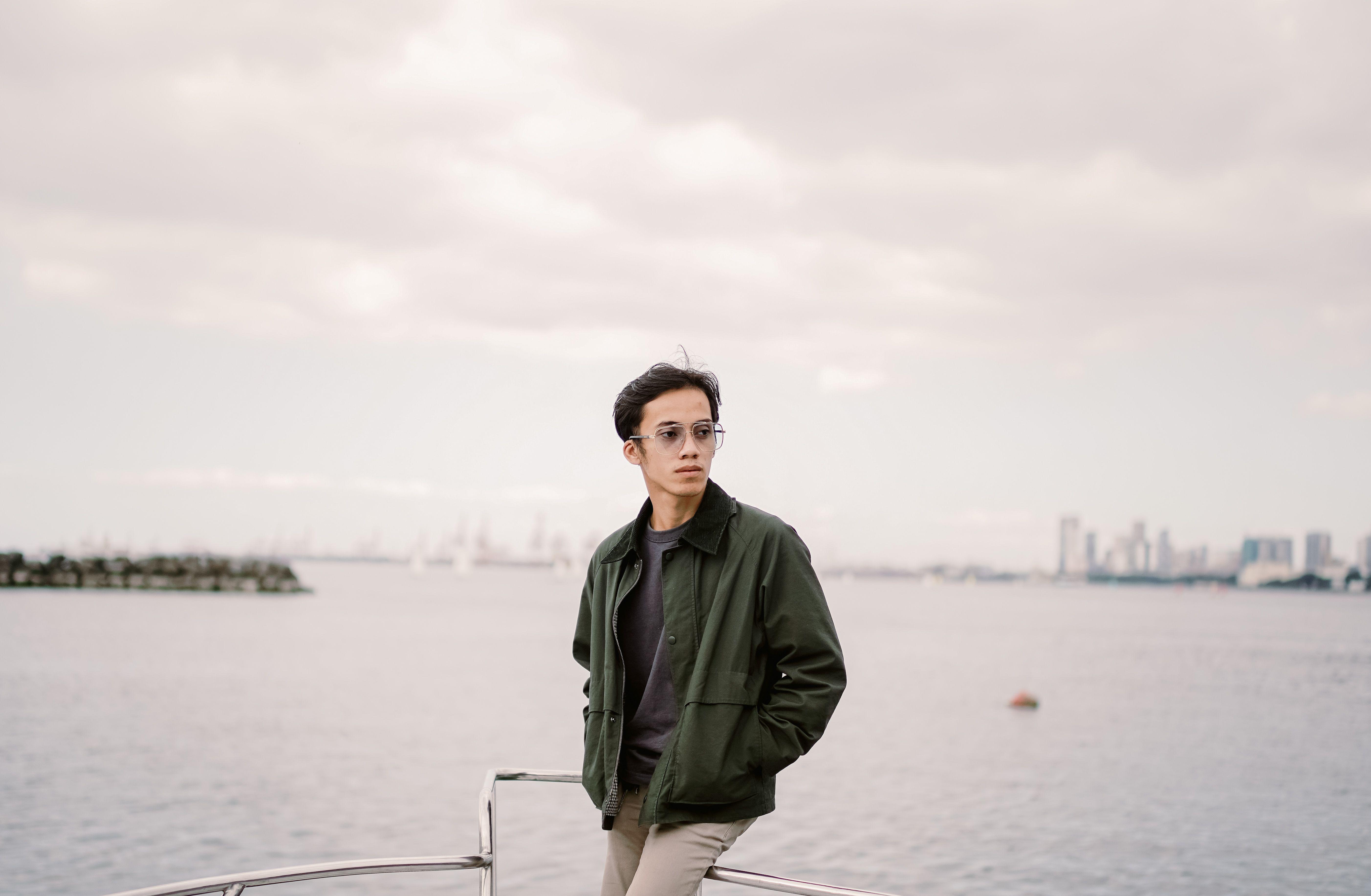 Young man in green jacket aboard a boat with city skyline in background.