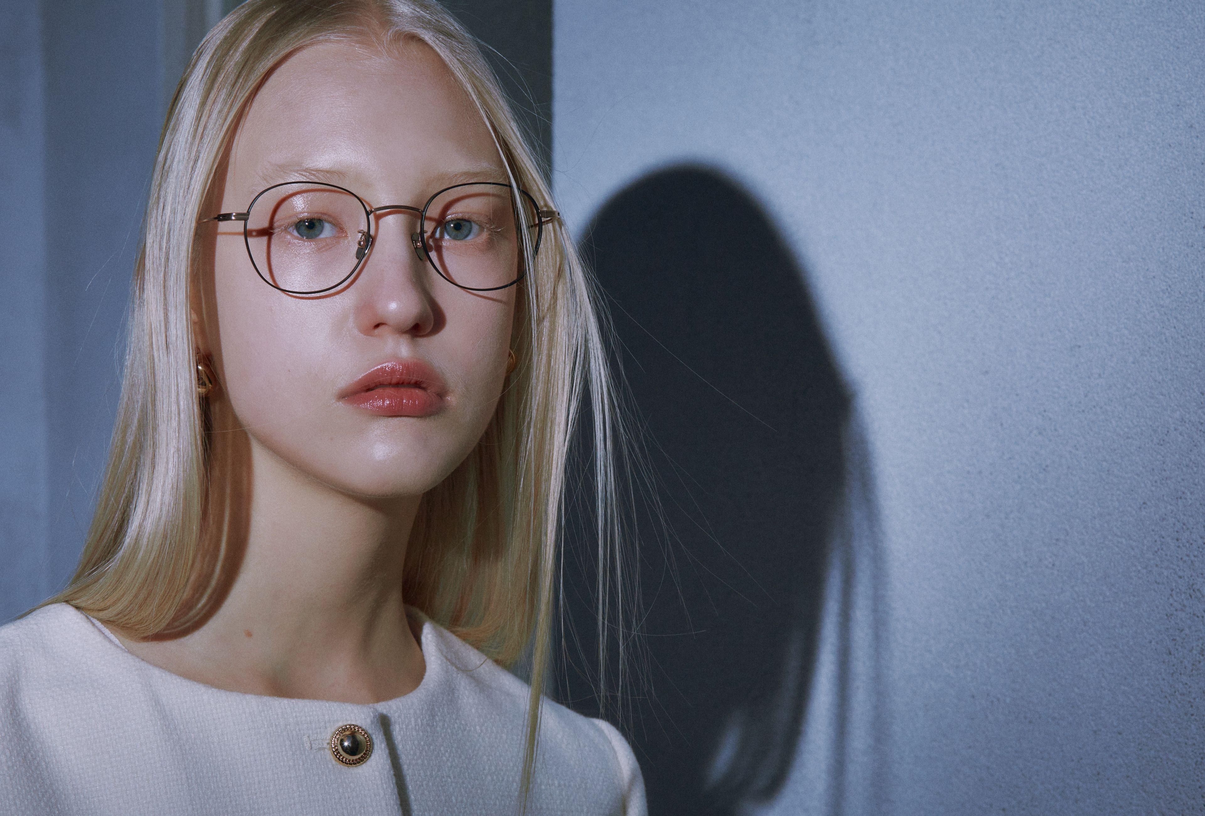 Portrait of a young woman wearing glasses with a significant shadow cast on the wall.