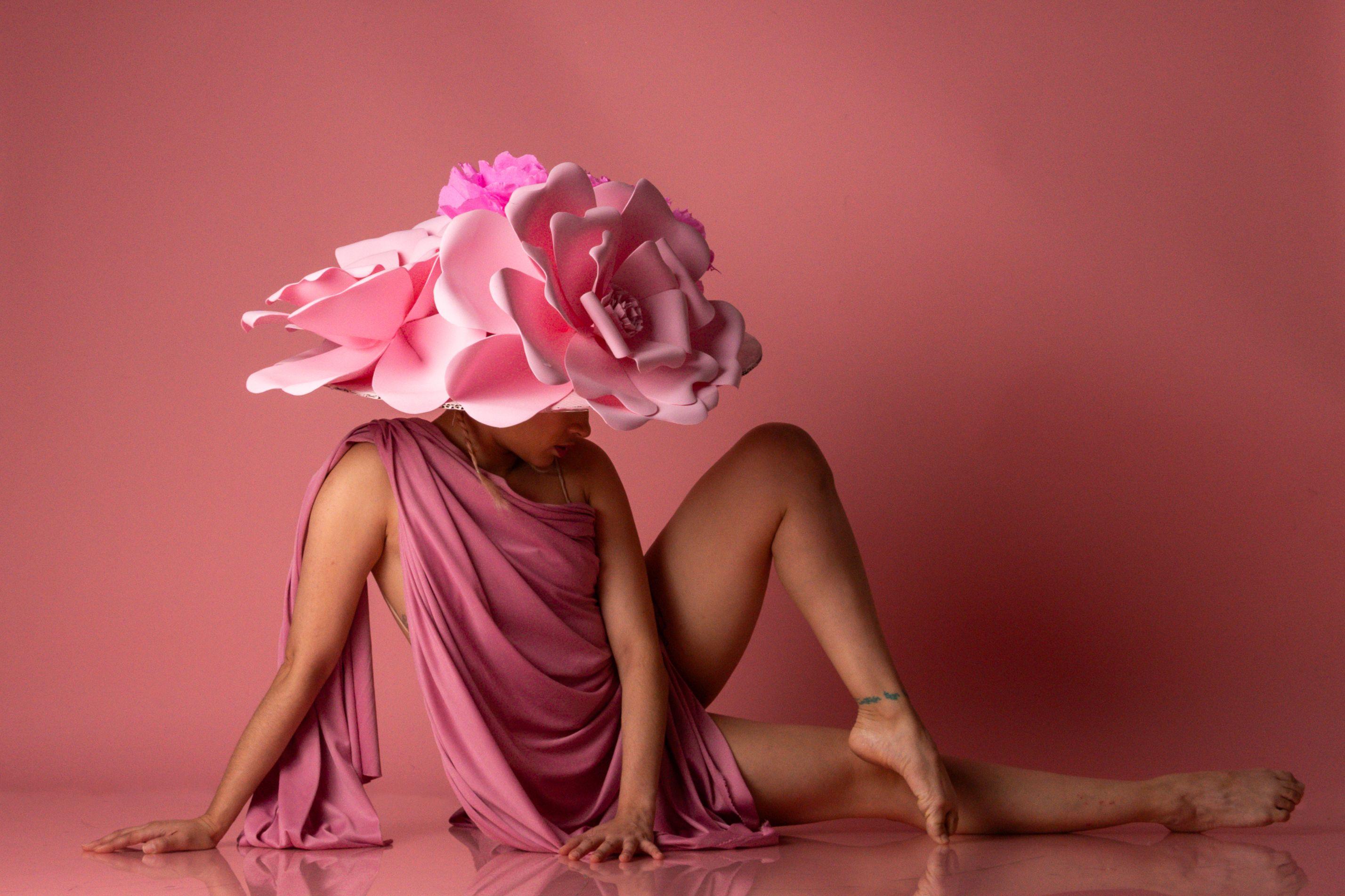 Artistic portrait of a female dancer in pink attire and a large floral hat, set against a pink backdrop.