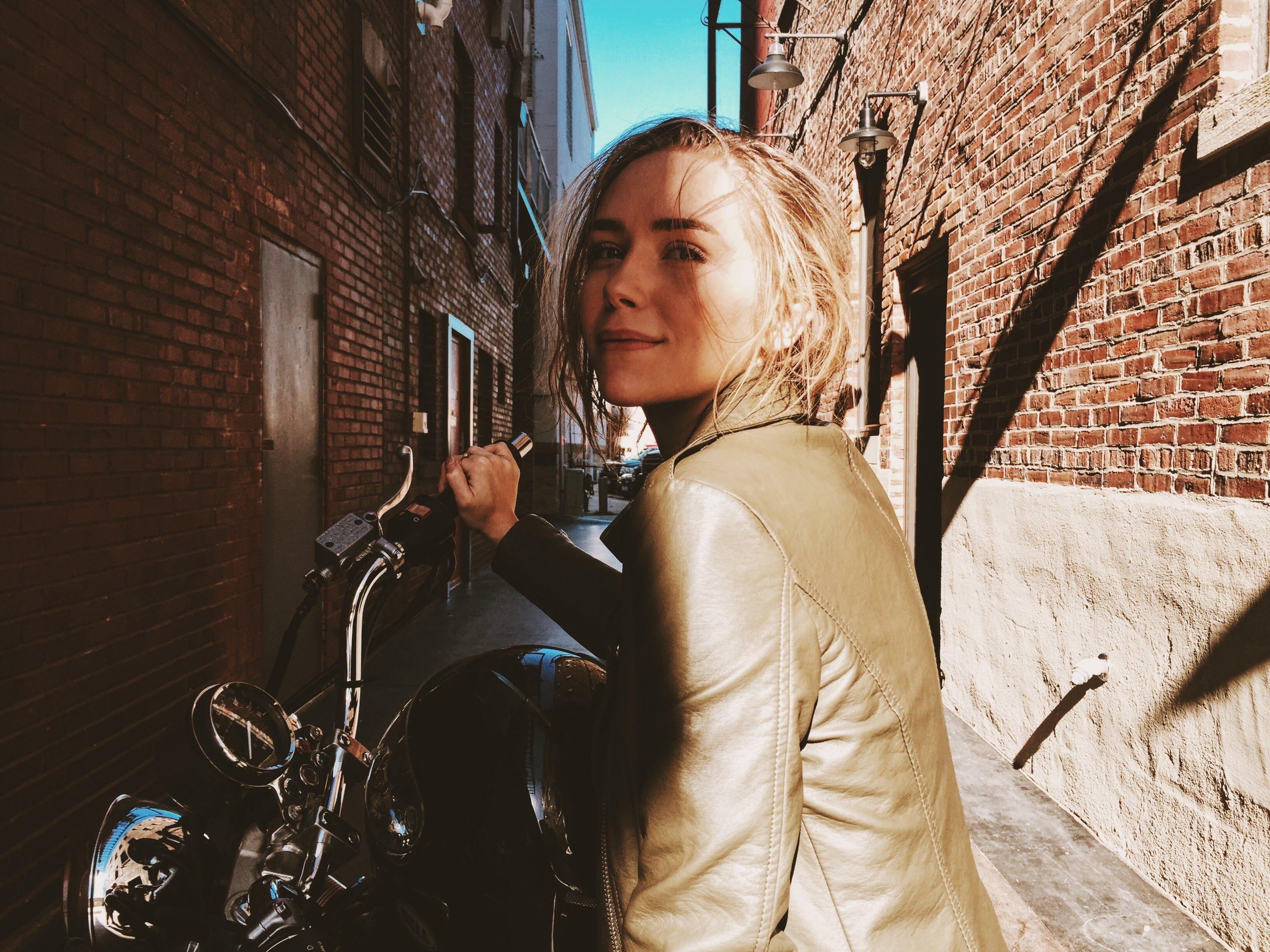 Confident woman in green leather jacket on motorcycle in Atlanta alleyway.