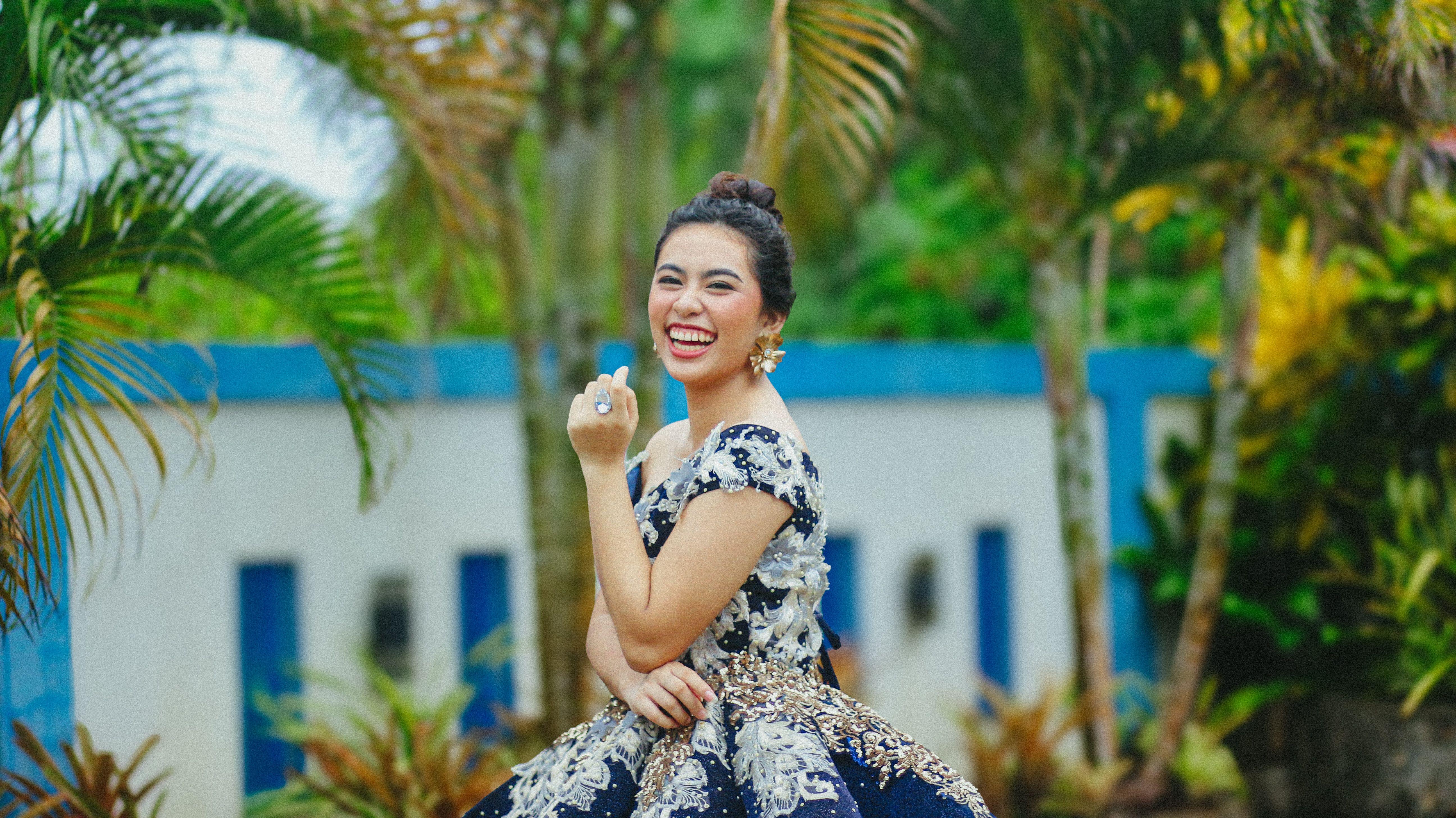 Happy woman in a luxurious dress laughing in a lush tropical setting.