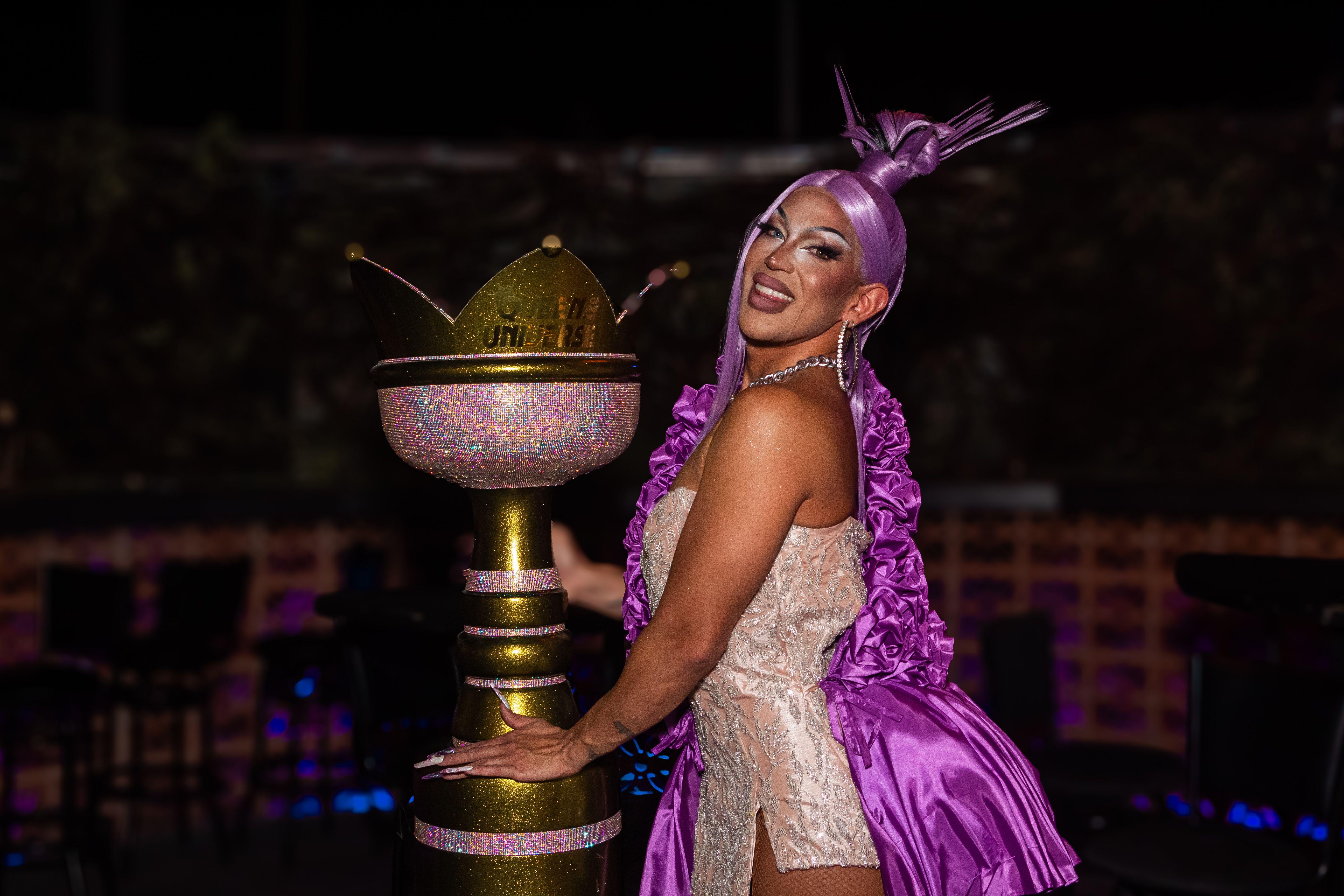 A vibrant performer in a purple outfit poses with a sparkling trophy during a night event.