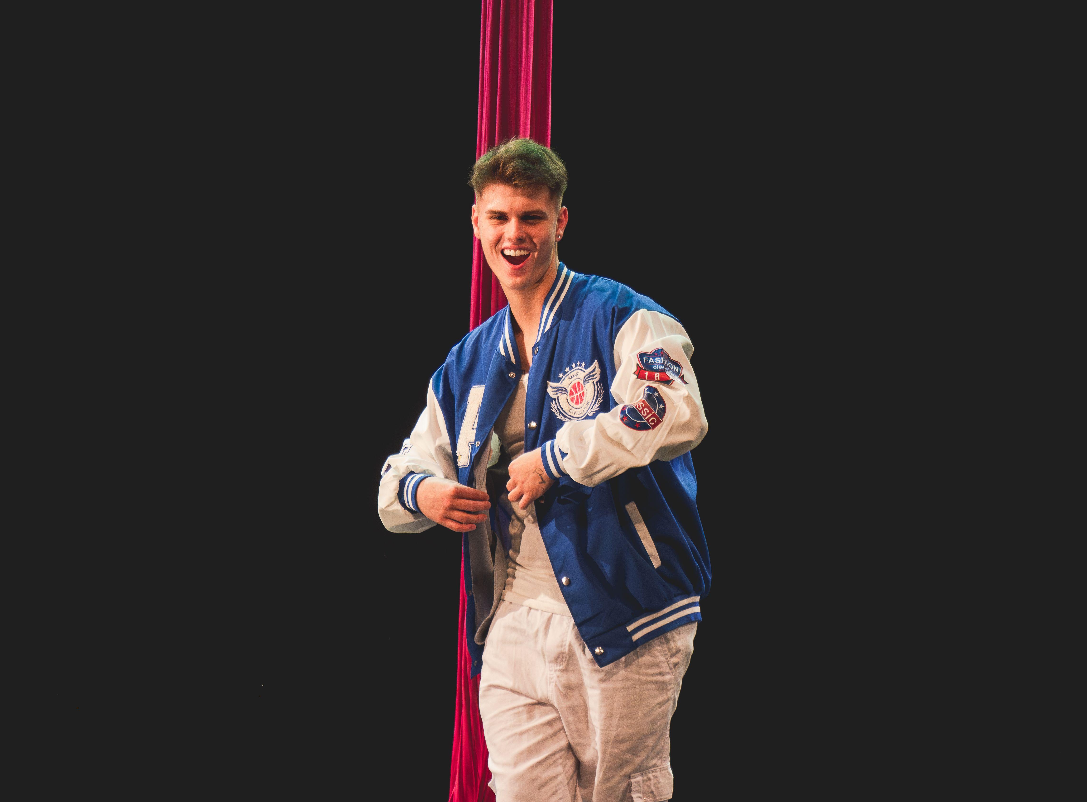 Teenager performing aerial dance in Brazil, wearing a blue jacket against a black background.