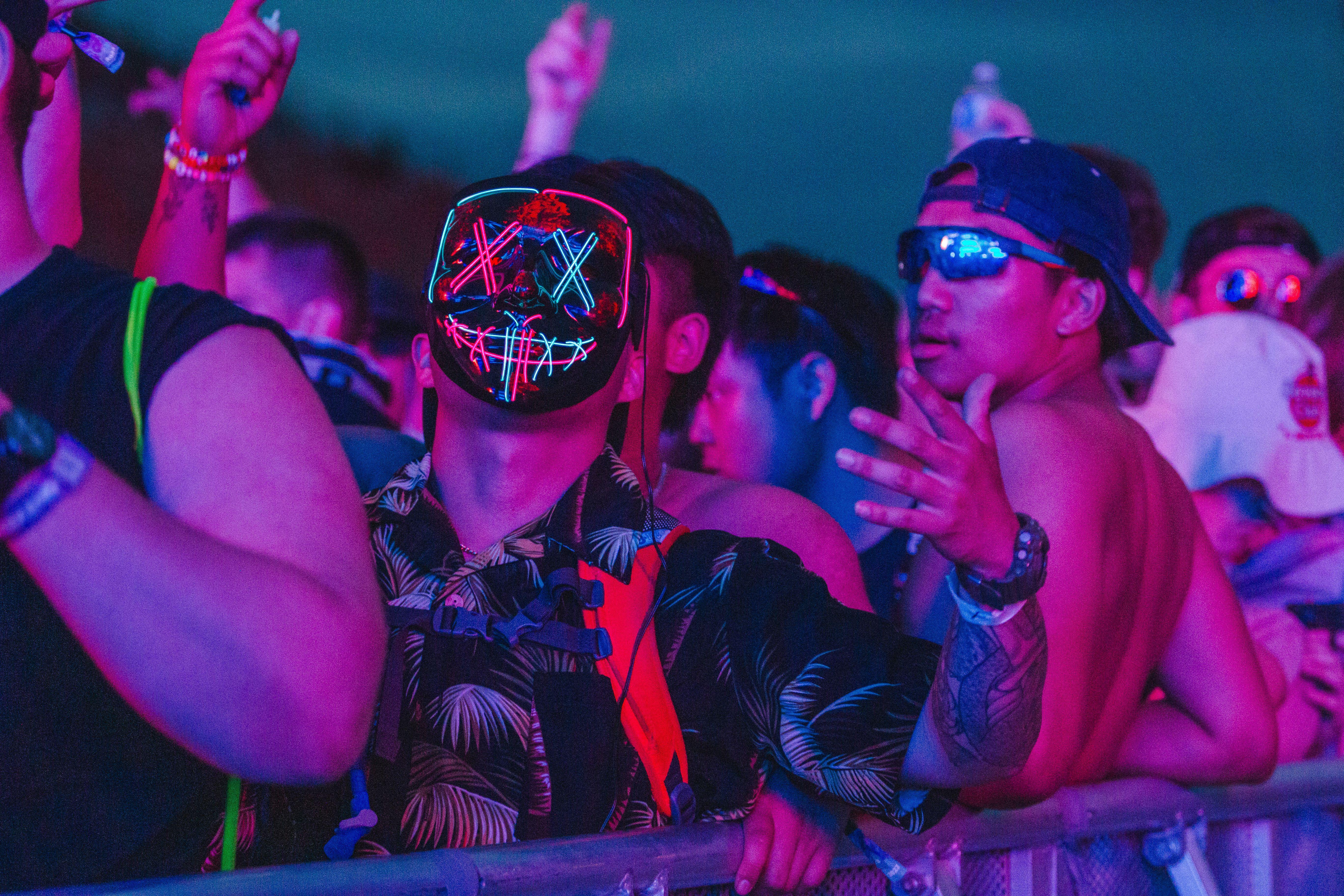 Energetic crowd with neon masks at an outdoor night festival, capturing the lively atmosphere.