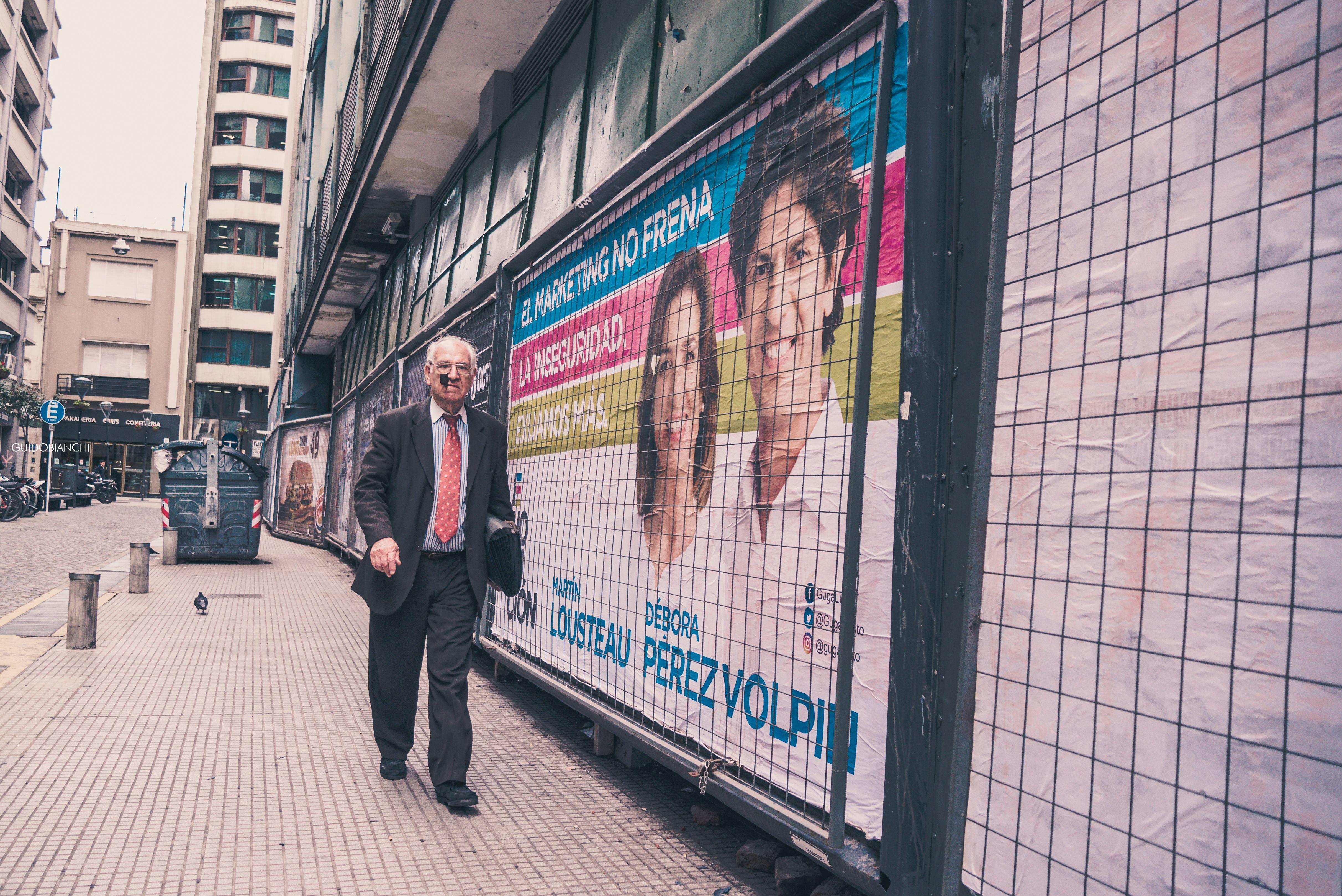 Elderly man walks past colorful political posters in an urban alleyway.