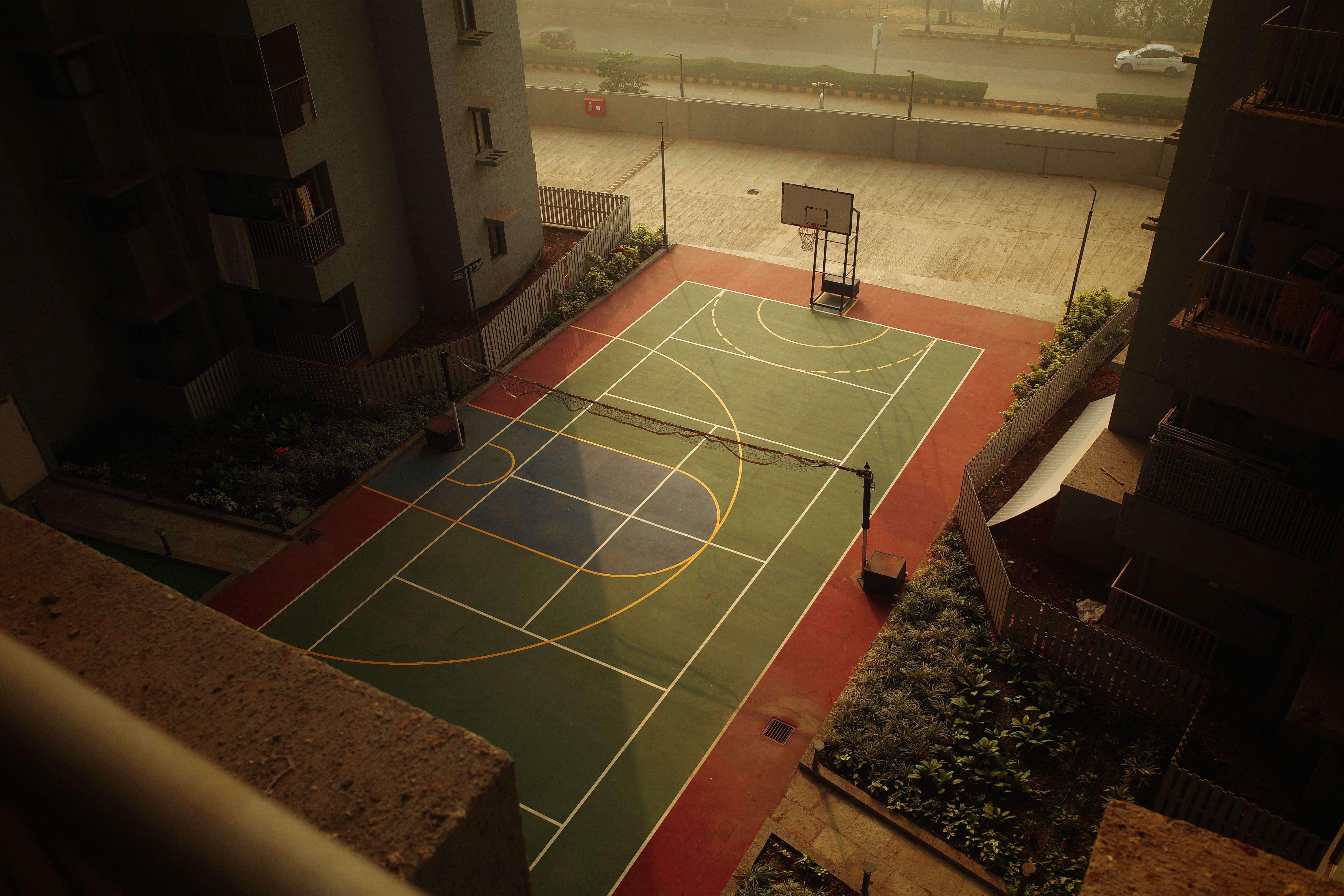 A peaceful urban sports court viewed from above during sunset, showcasing a basketball hoop and tennis lines.