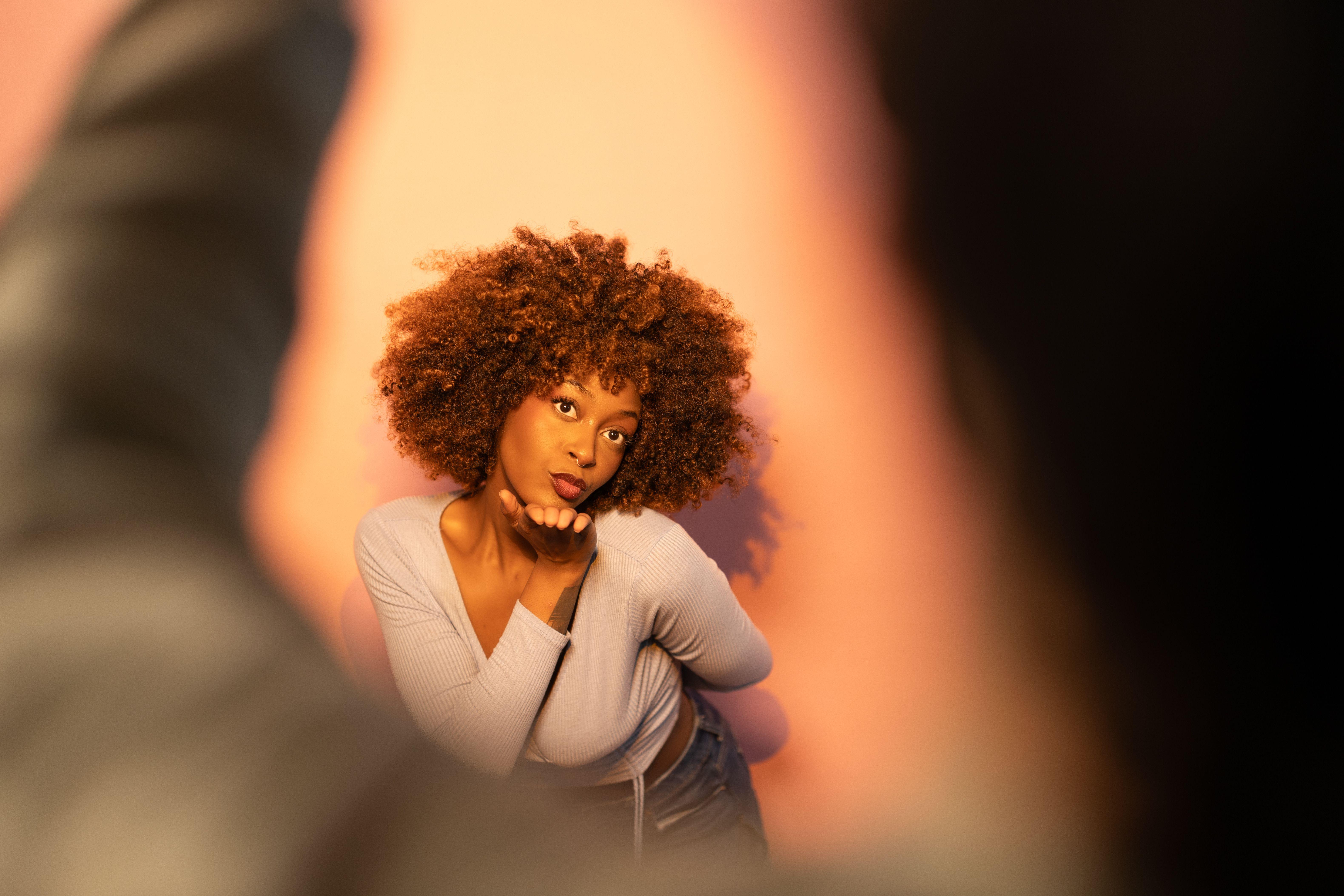A woman blowing a kiss with dramatic lighting and warm background.