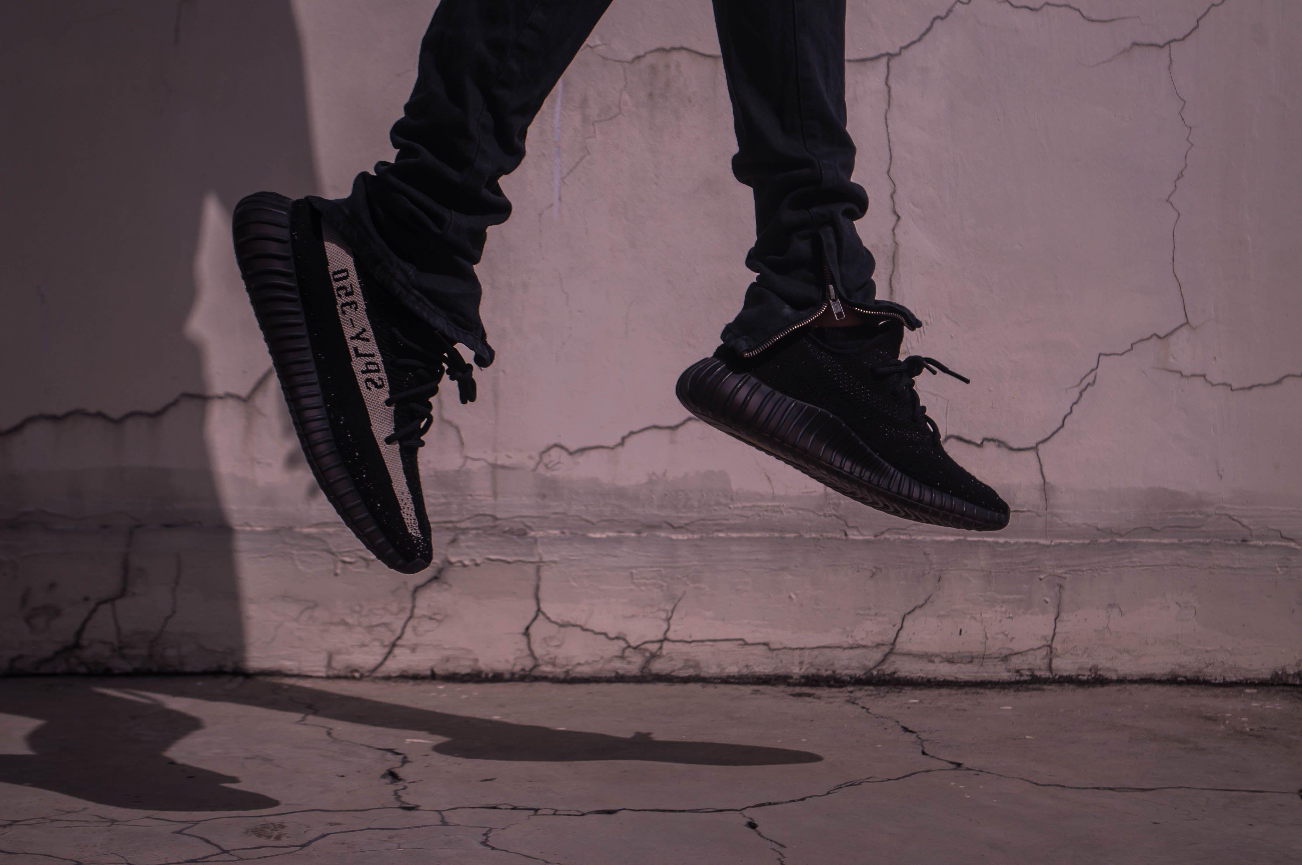 A stylish and dynamic urban photo capturing black sneakers in mid-jump against a cracked concrete wall.