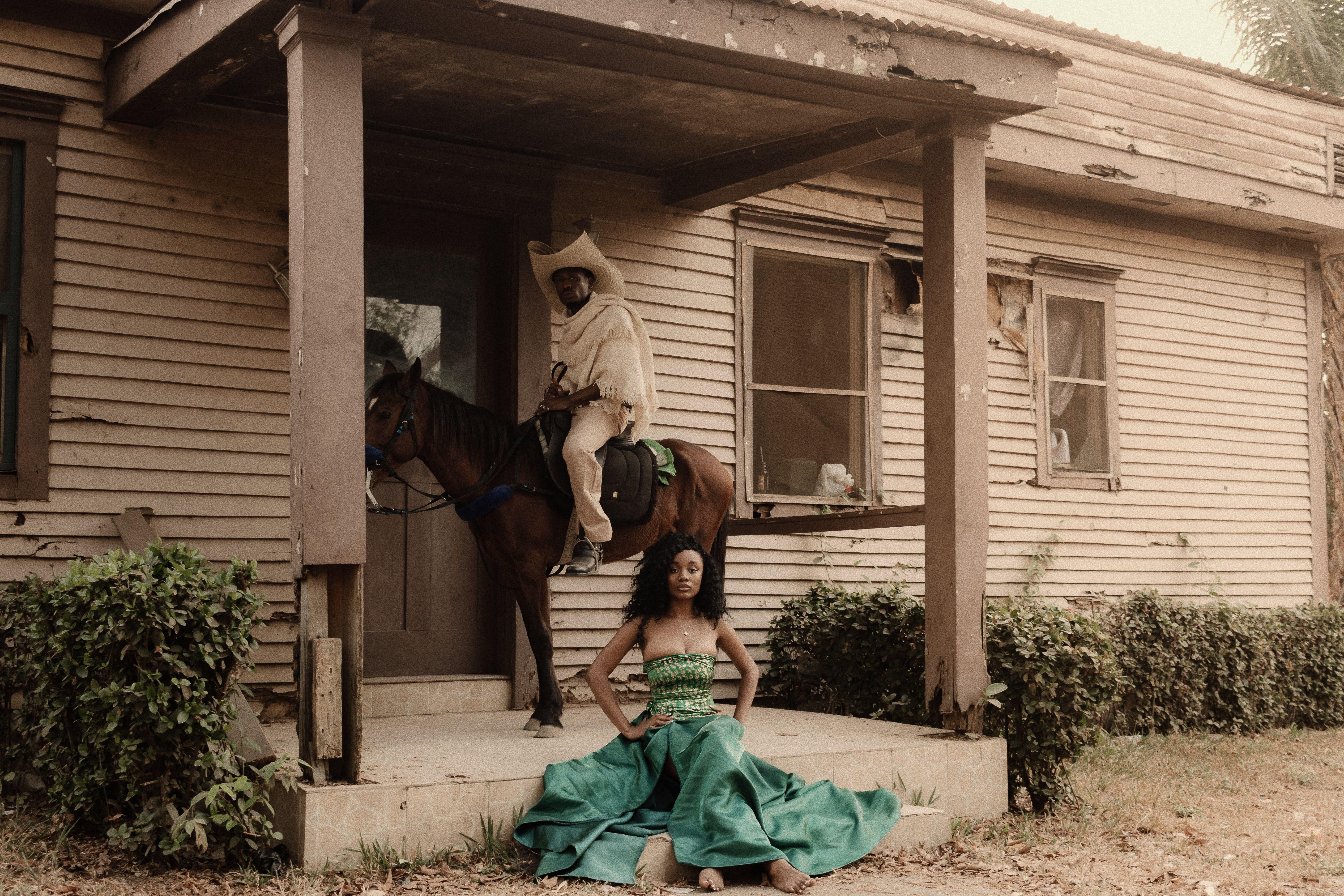 Man on horseback and woman in traditional dress outside a rustic building in Nigeria.