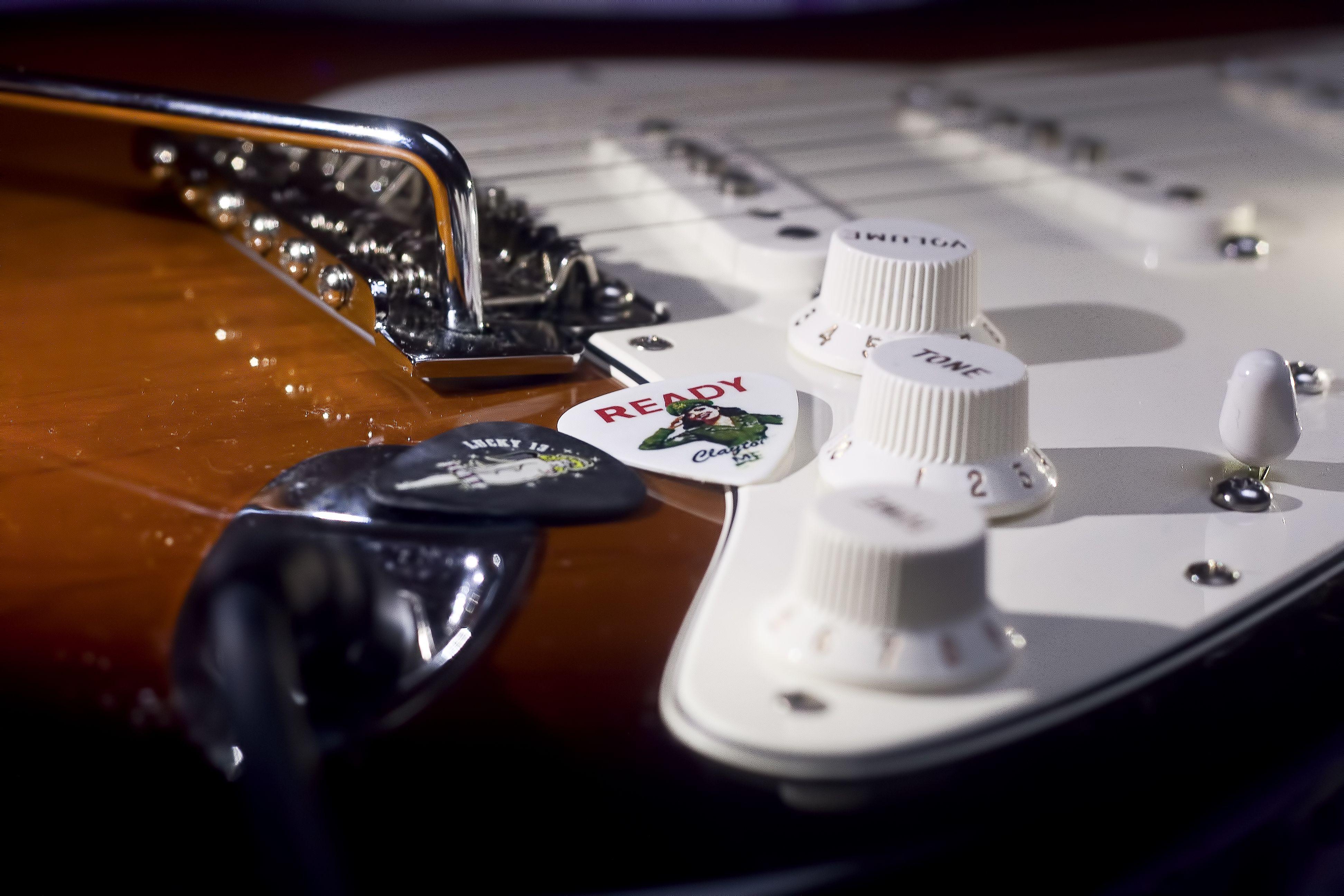 Detailed view of electric guitar showing control knobs, picks, and bridge in focus.