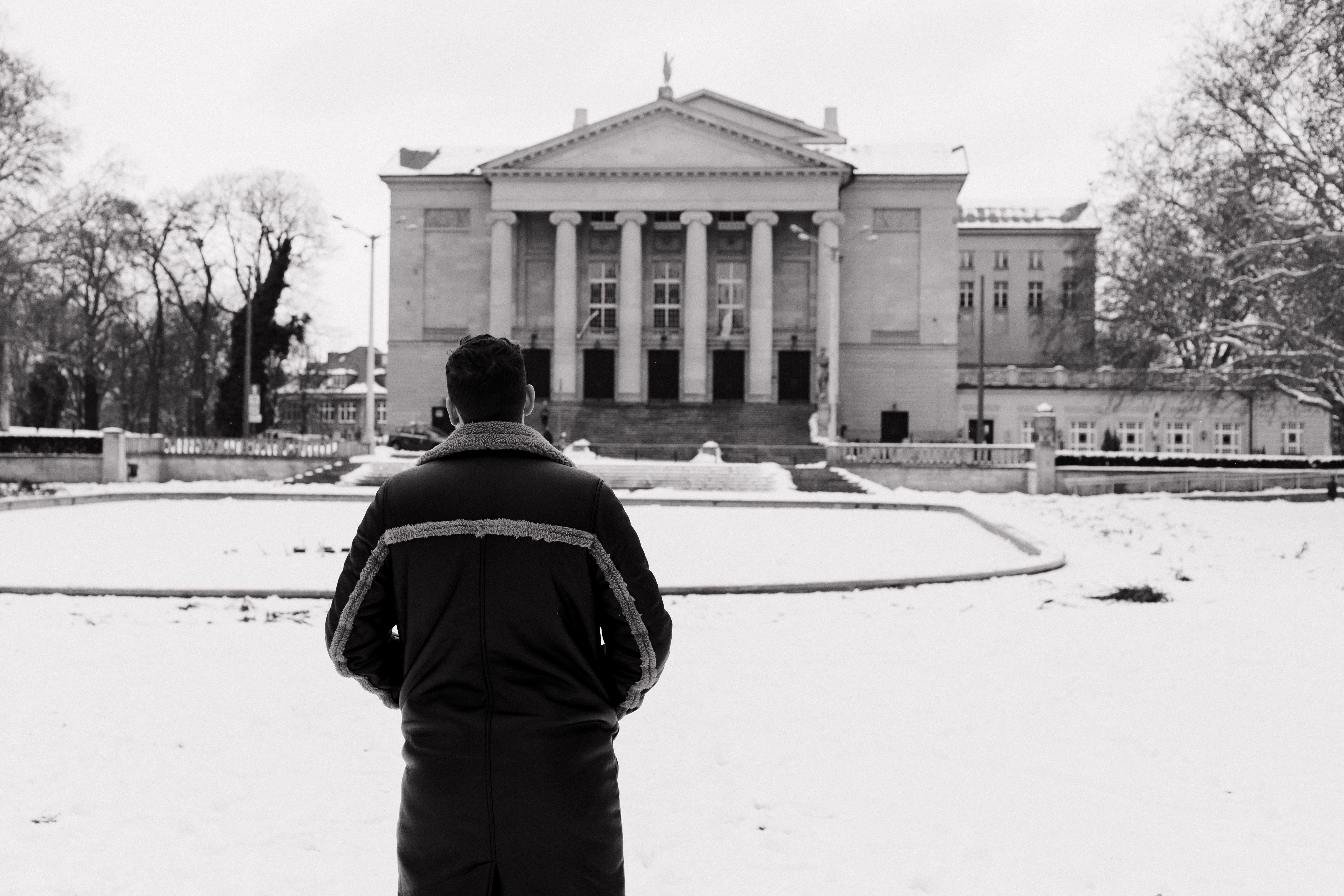Man standing before Poznań Opera House in winter, showcasing architecture amidst snowy surroundings.