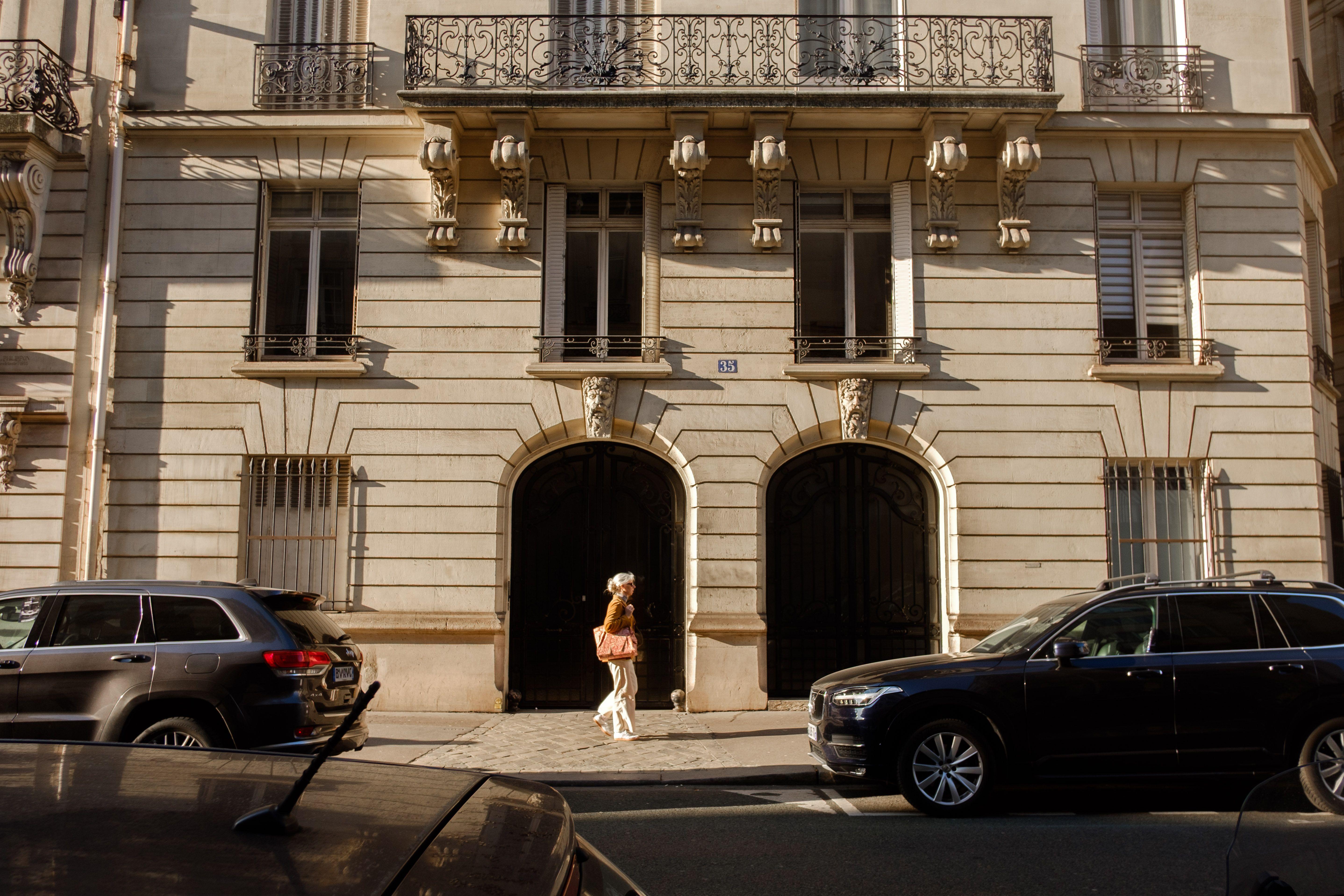 A woman walking by elegant Parisian architecture on a sunny day.