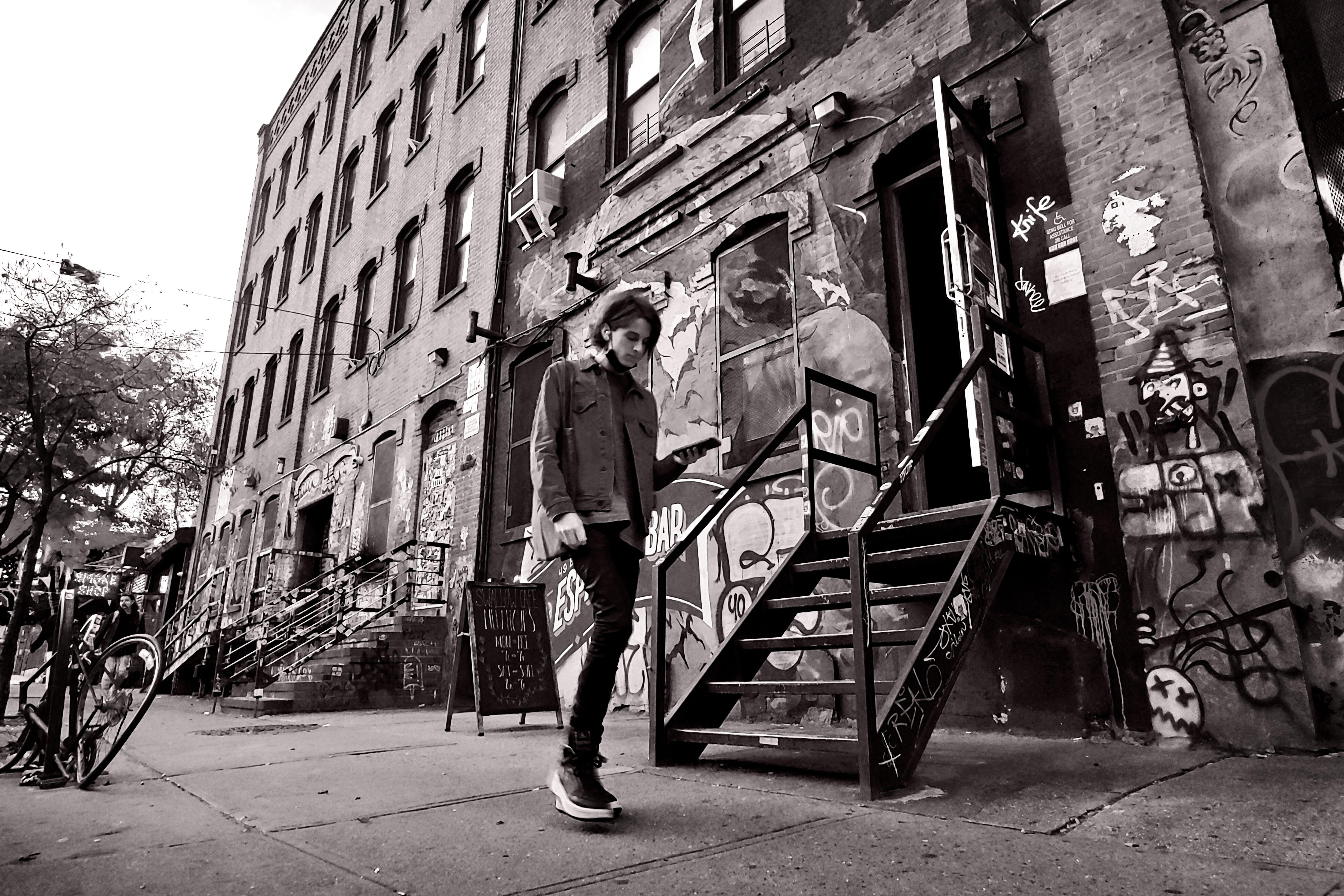 Black and white photo of a person walking in Brooklyn's graffiti-filled street, showcasing urban art and architecture.
