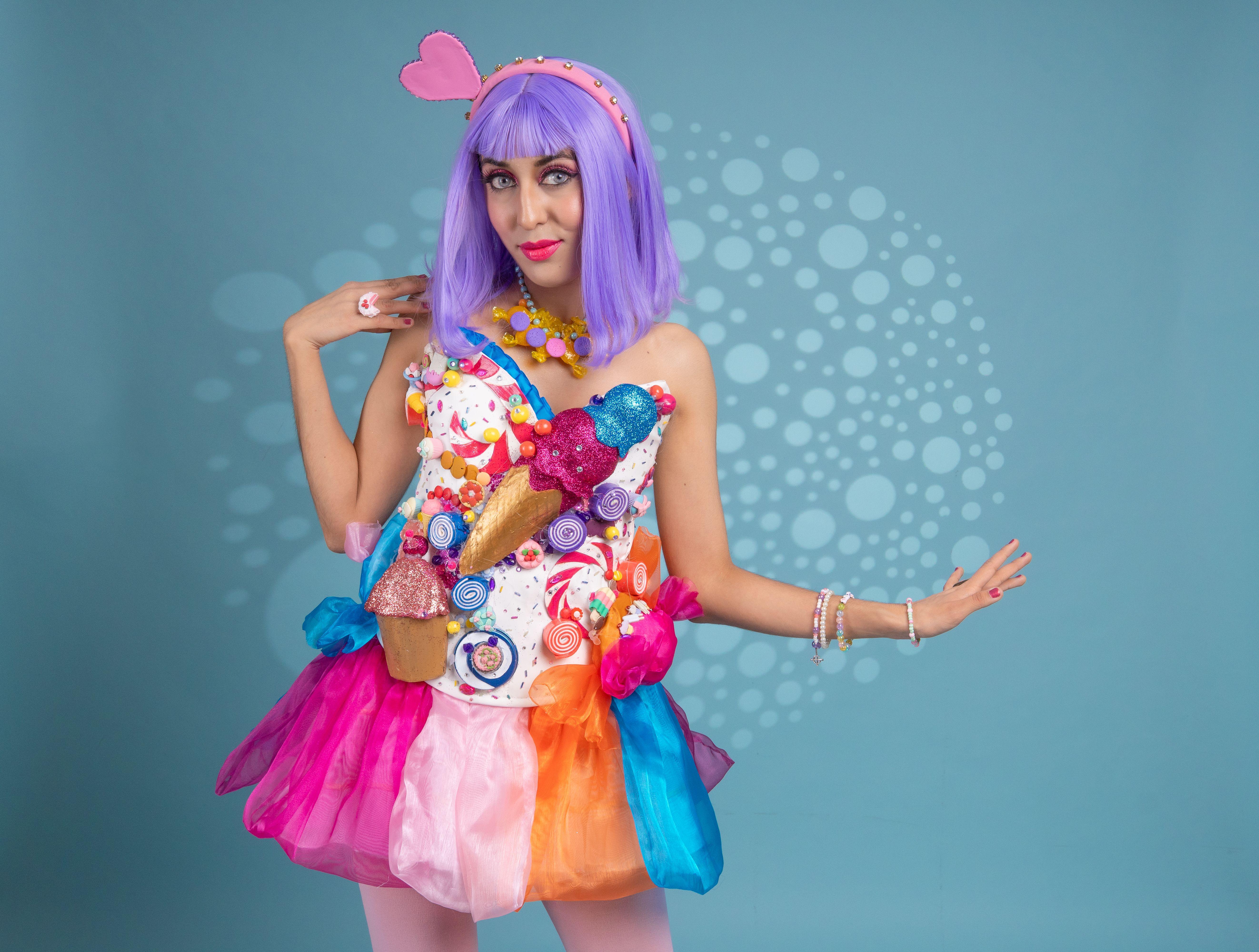 Colorful artistic cosplay woman in candy-themed costume on blue background.
