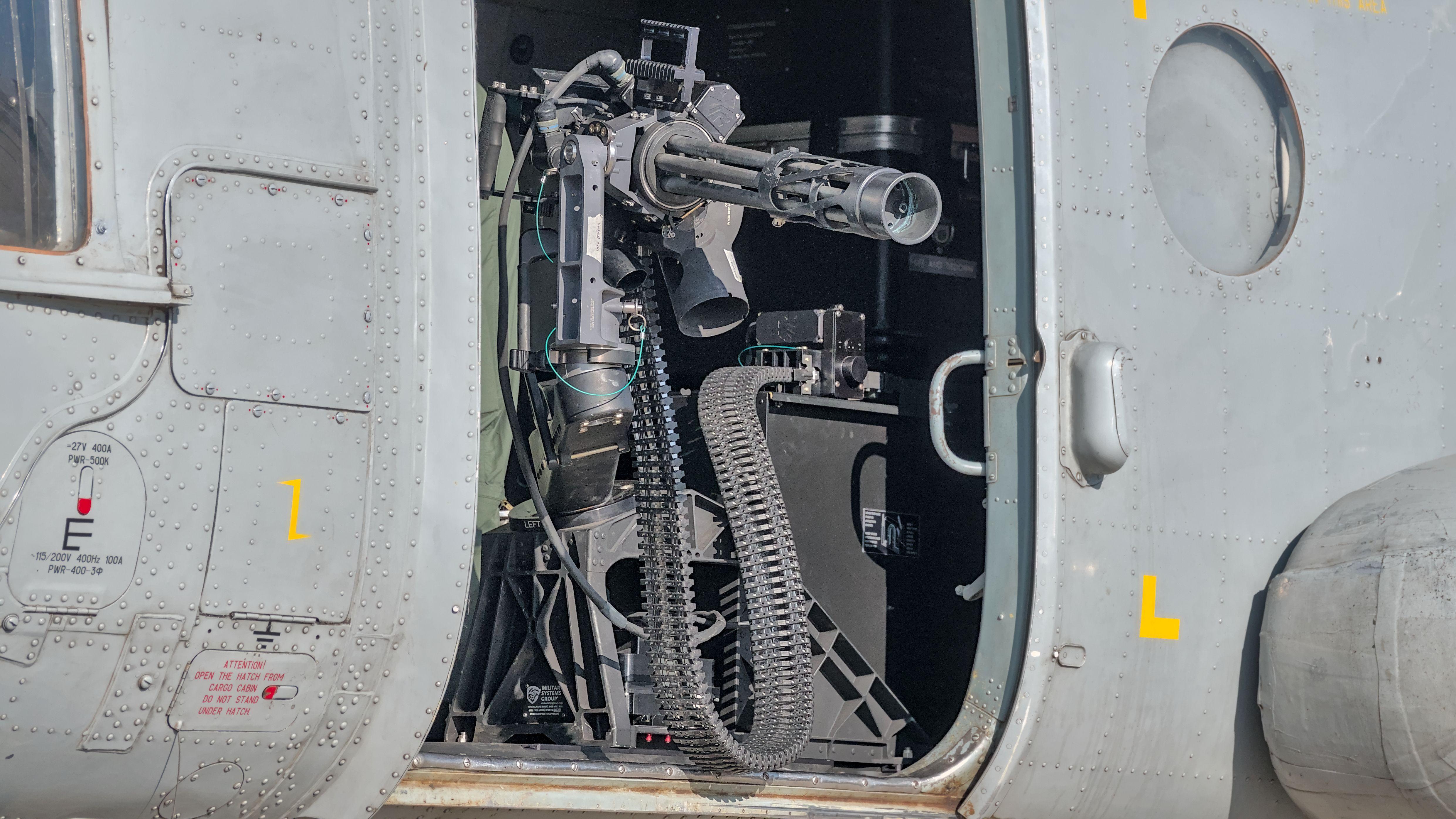 Close-up of a helicopter gun turret, showcasing detailed weaponry in bright sunlight.