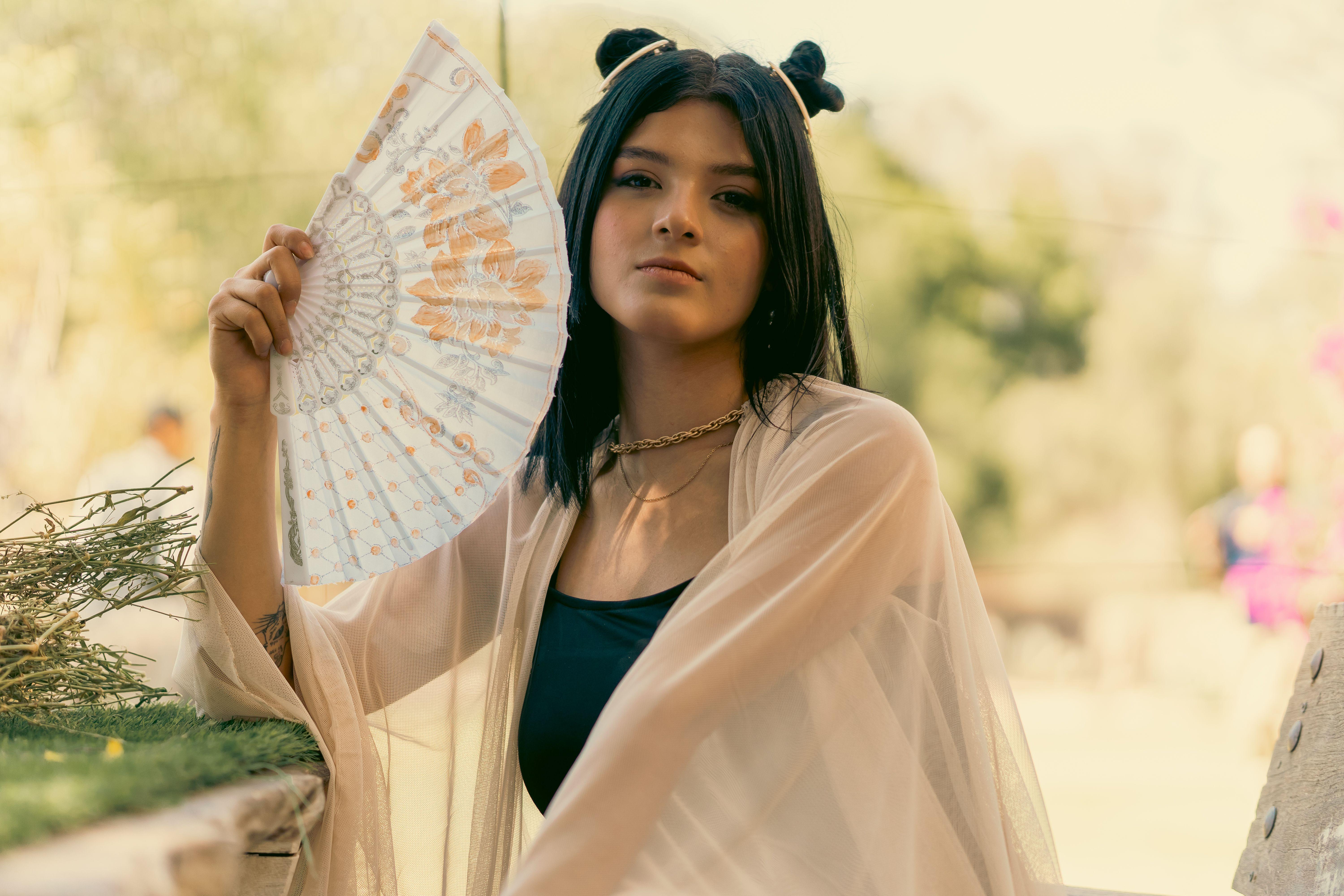 A young woman with a fan poses outdoors in Leon, Guanajuato, Mexico, exuding elegance.