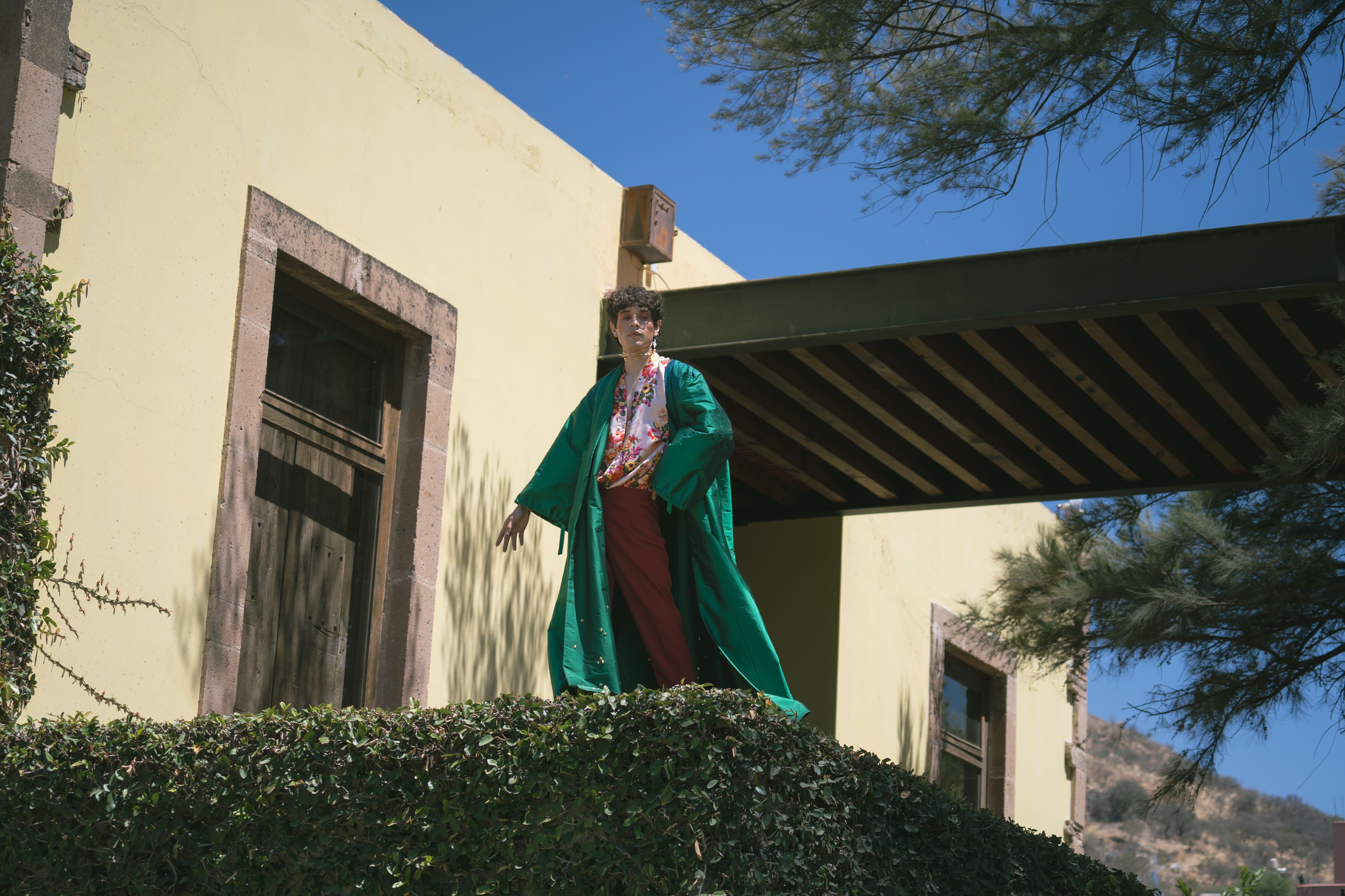 A person in a vibrant kimono poses elegantly outdoors against an architectural backdrop.
