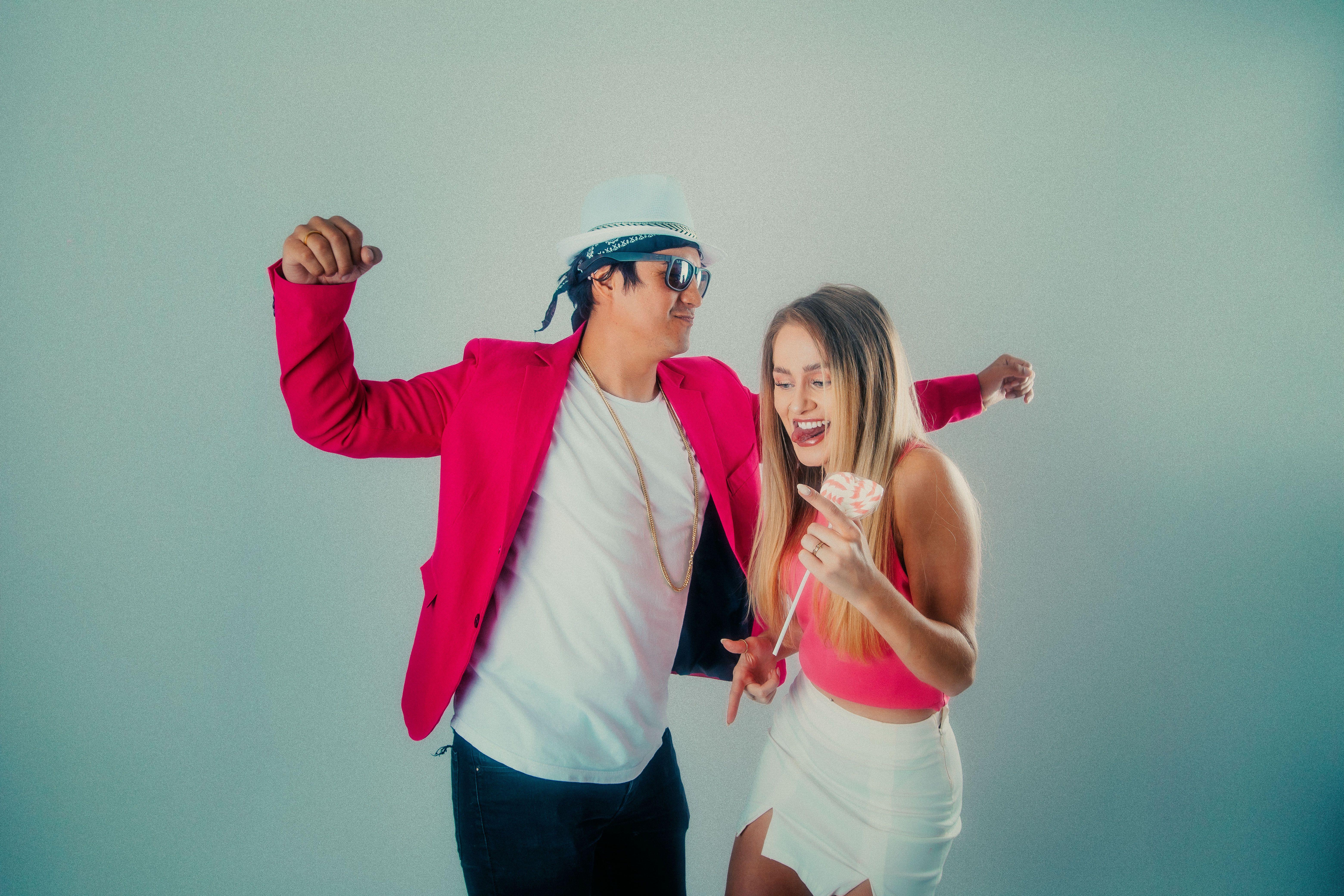 A lively couple dancing indoors, dressed in stylish pink attire, exuding joy and energy.