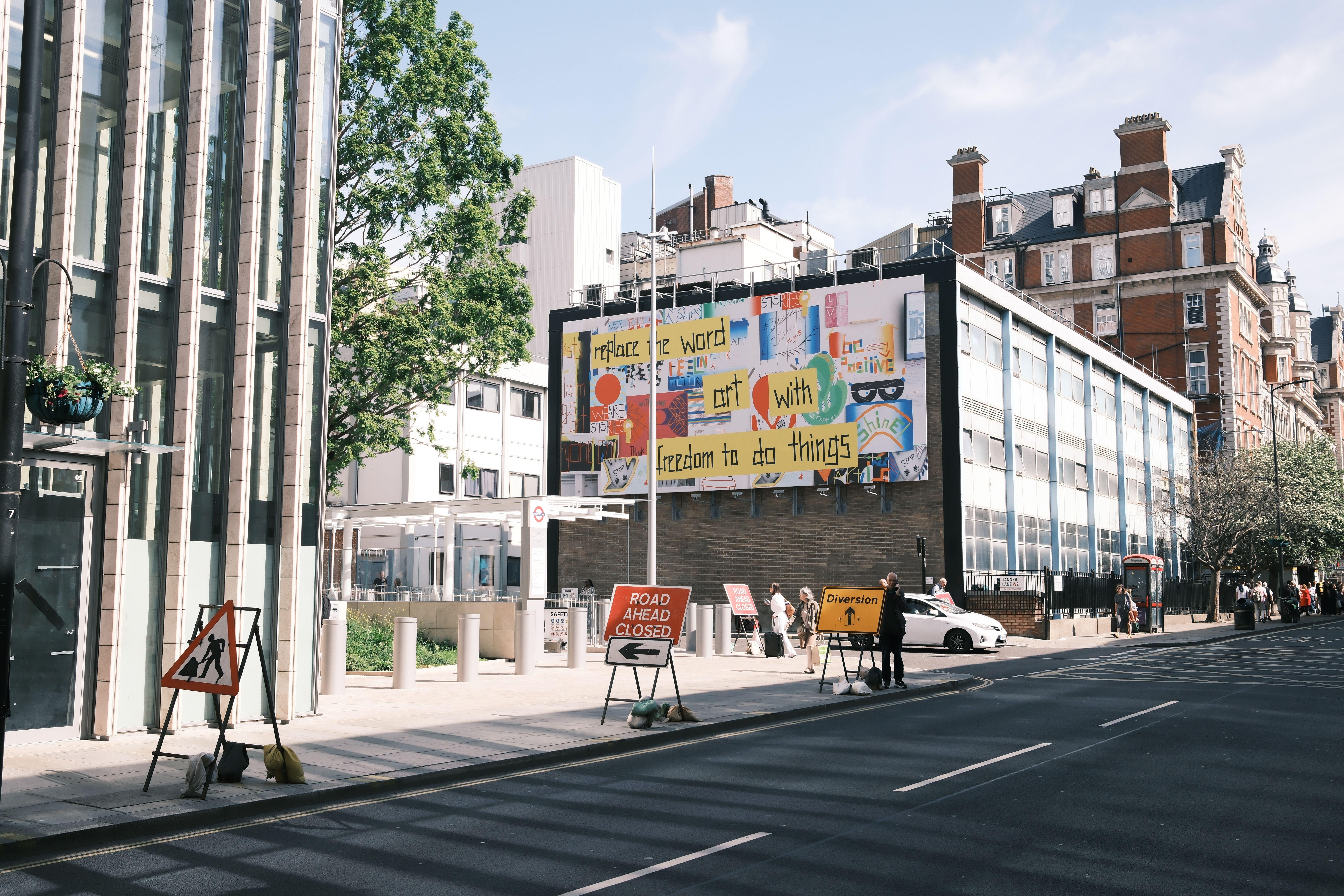 City street scene with a colorful billboard and road closure signs.