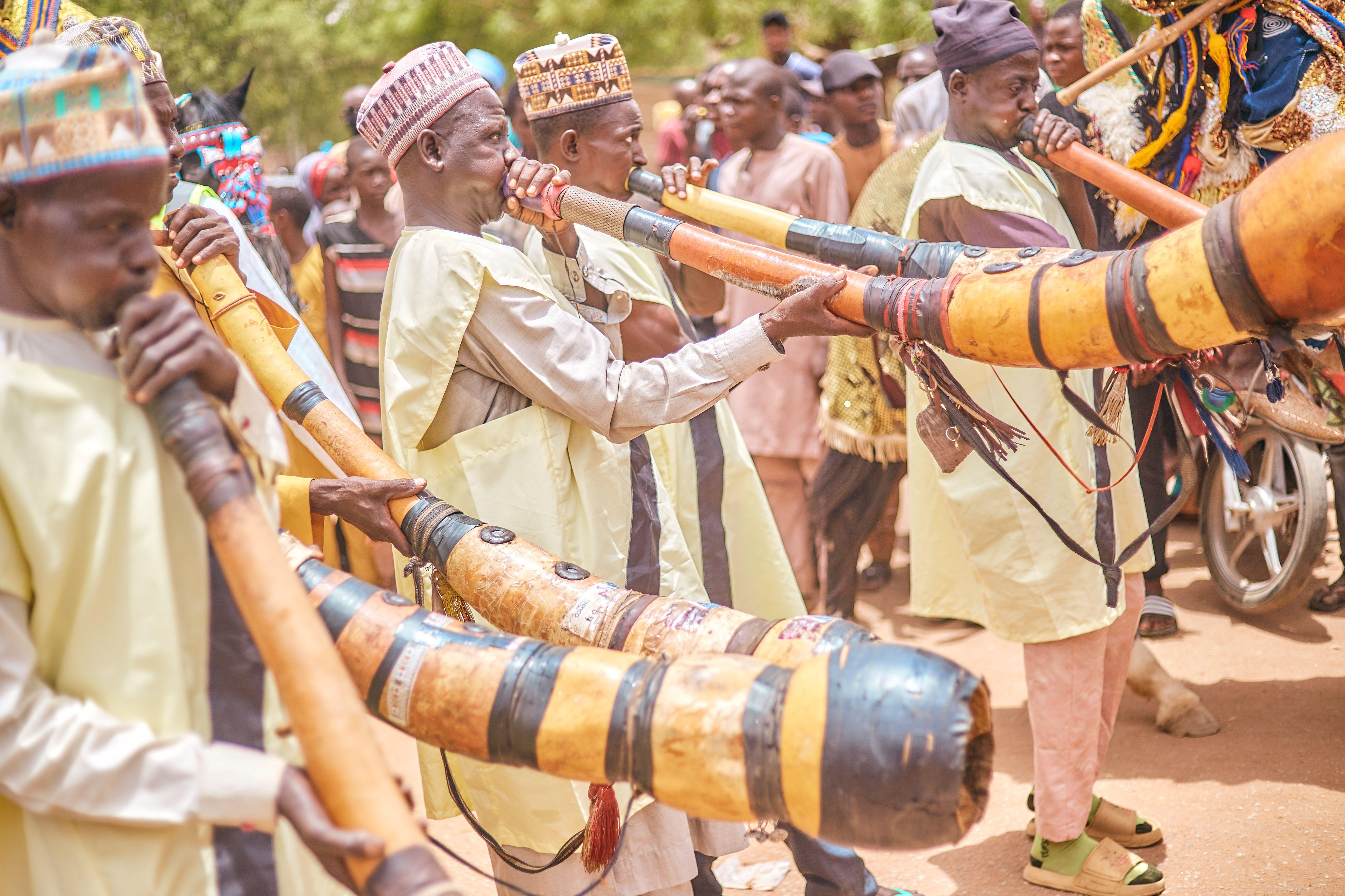Colorful celebration with musicians playing traditional African horns at an outdoor cultural festival.
