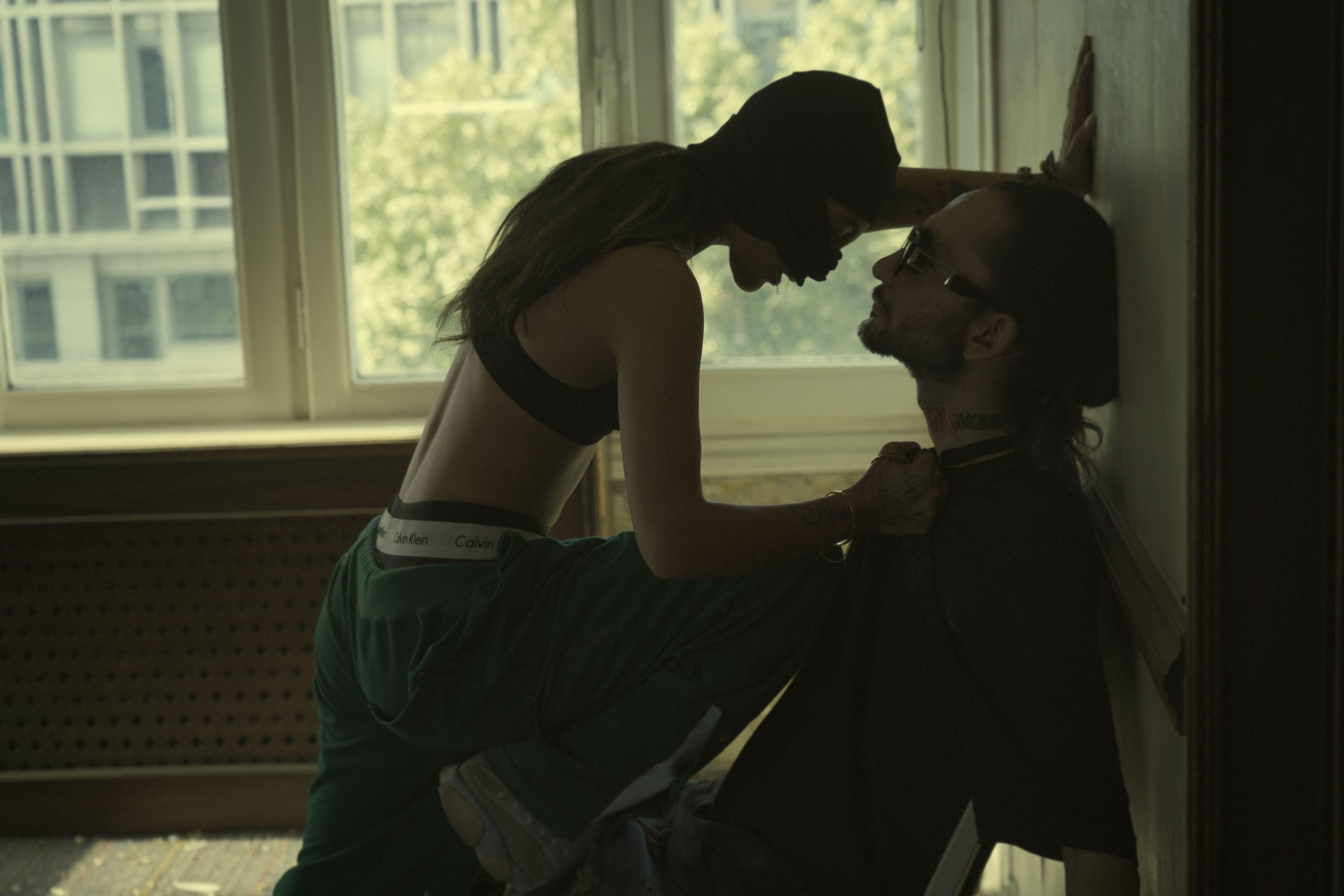 A dramatic urban encounter between two people by a window in a dimly lit room.